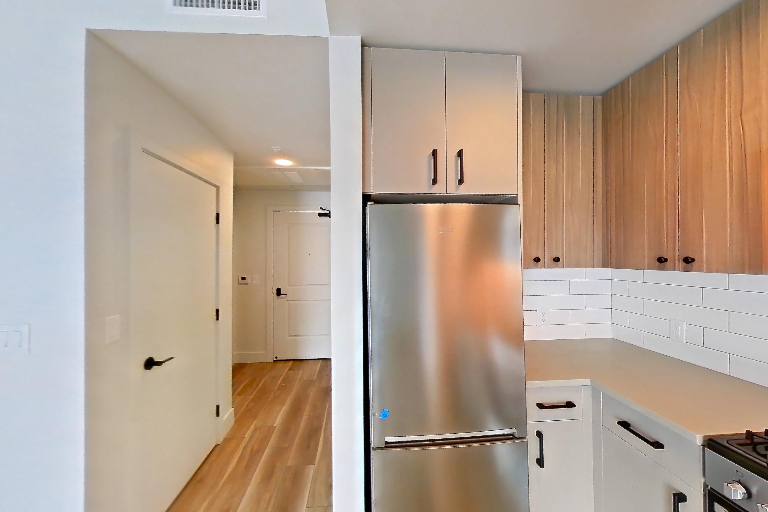 Kitchen with dishwasher, gas range, light countertops, light wood-finish flooring, oven/range, refrigerator, and stainless steel appliances, Apartment 445 at The Myles