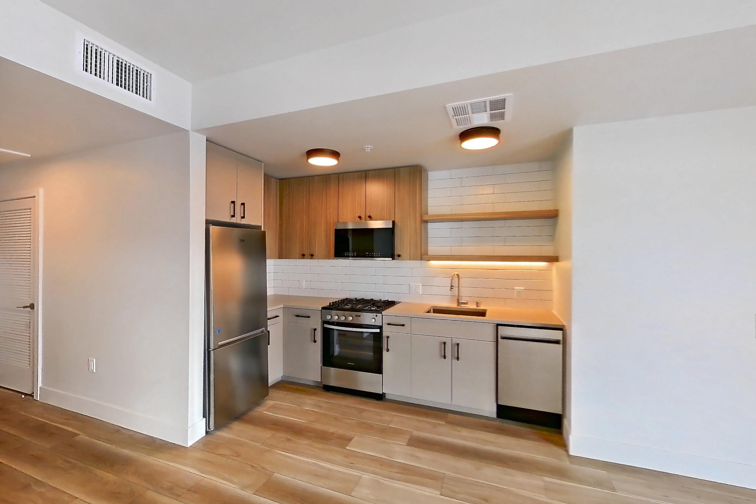 Living space with dishwasher, gas range, light stone countertops, light wood-finish flooring, oven/range, stainless steel appliances, and wood-look tile flooring, Apartment 445 at The Myles
