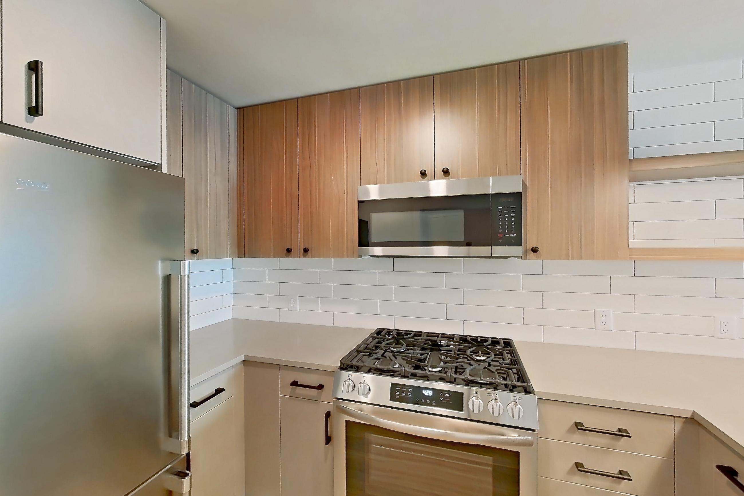 Kitchen with dishwasher, gas range, light countertops, light wood-finish flooring, microwave, oven/range, refrigerator, and stainless steel appliances, Apartment 447 at The Myles