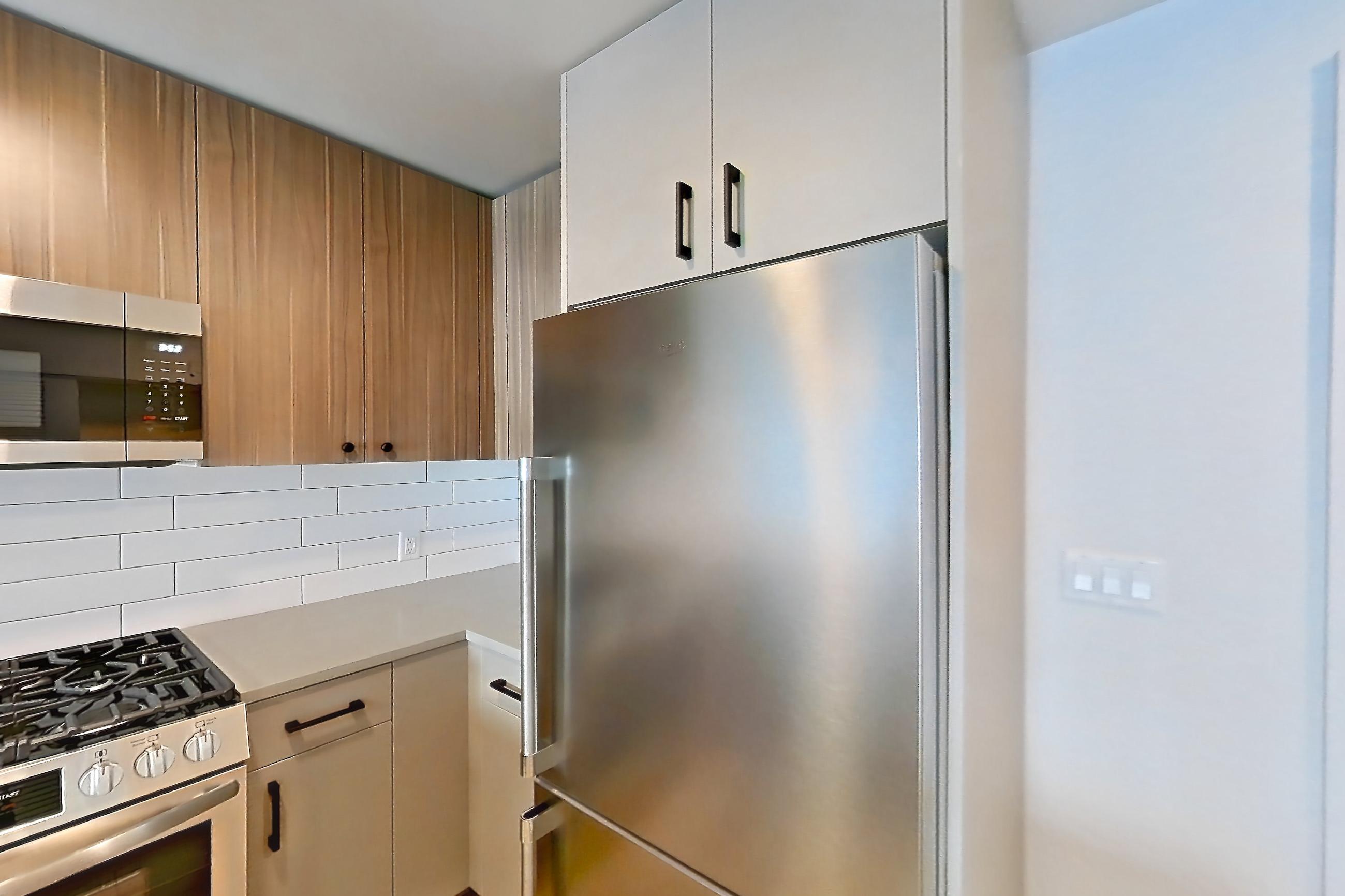 Kitchen with dishwasher, gas range, light countertops, light wood-finish flooring, microwave, oven/range, refrigerator, and stainless steel appliances, Apartment 448 at The Myles