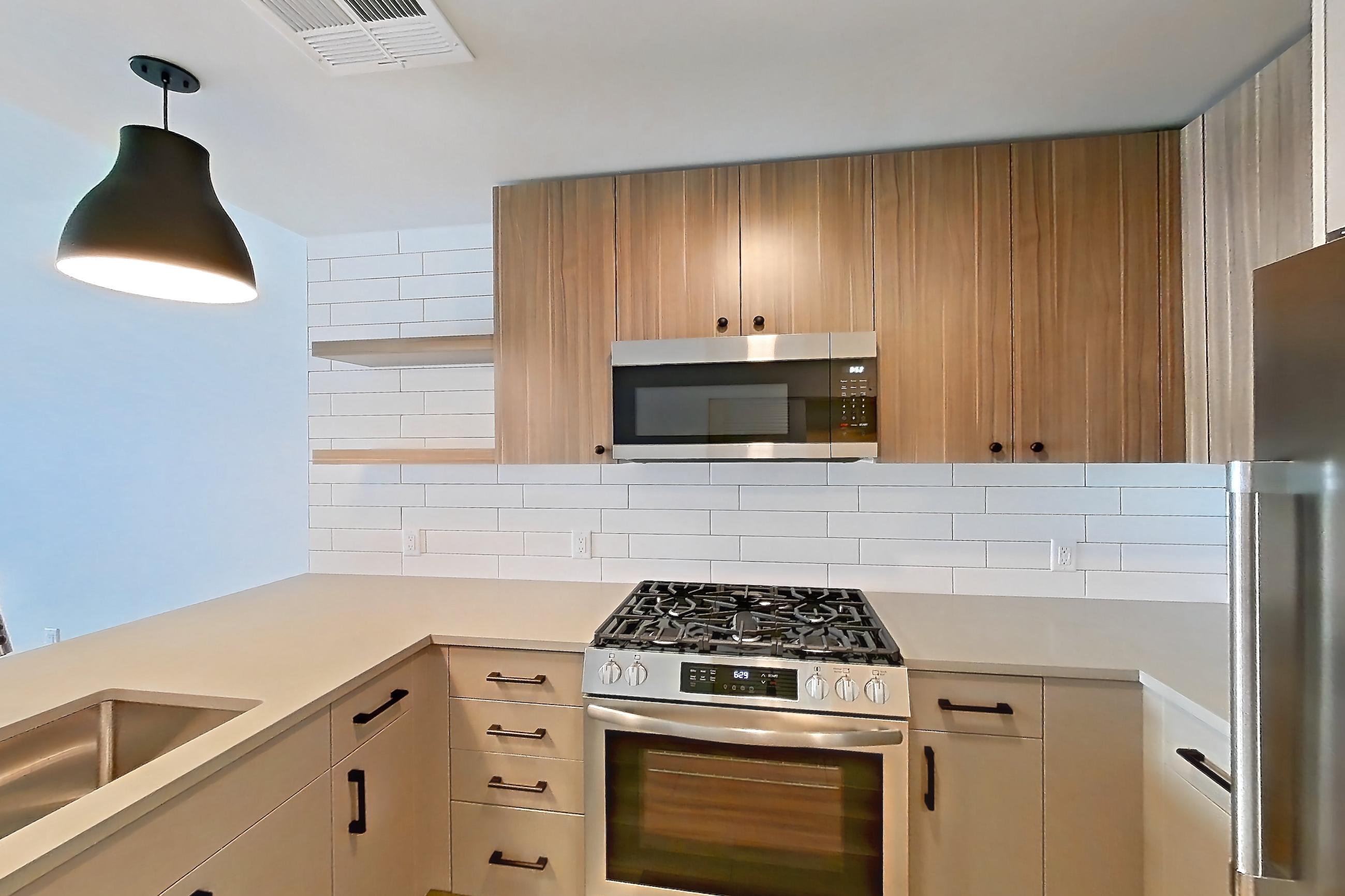 Kitchen with dishwasher, gas range, light countertops, light wood-finish flooring, microwave, oven/range, refrigerator, and stainless steel appliances, Apartment 448 at The Myles