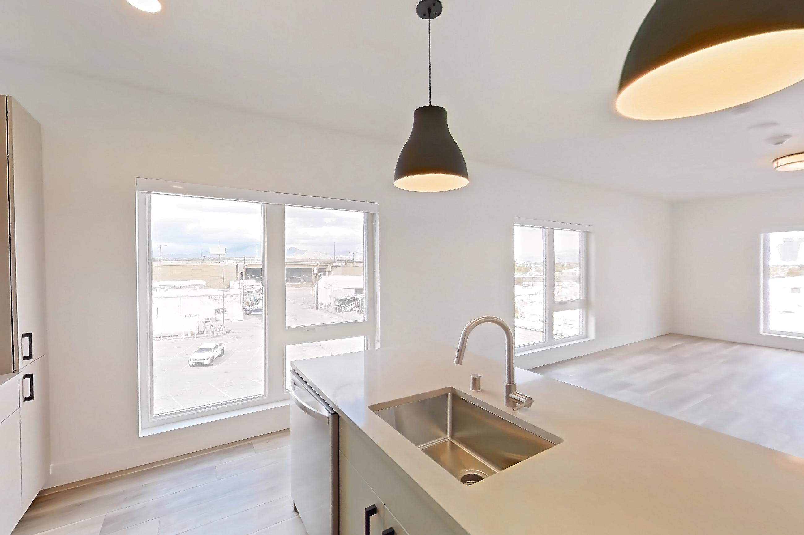 Kitchen with gas range, kitchen island, light countertops, light stone countertops, light wood-finish flooring, microwave, oven/range, refrigerator, and stainless steel appliances, Apartment 449 at The Myles