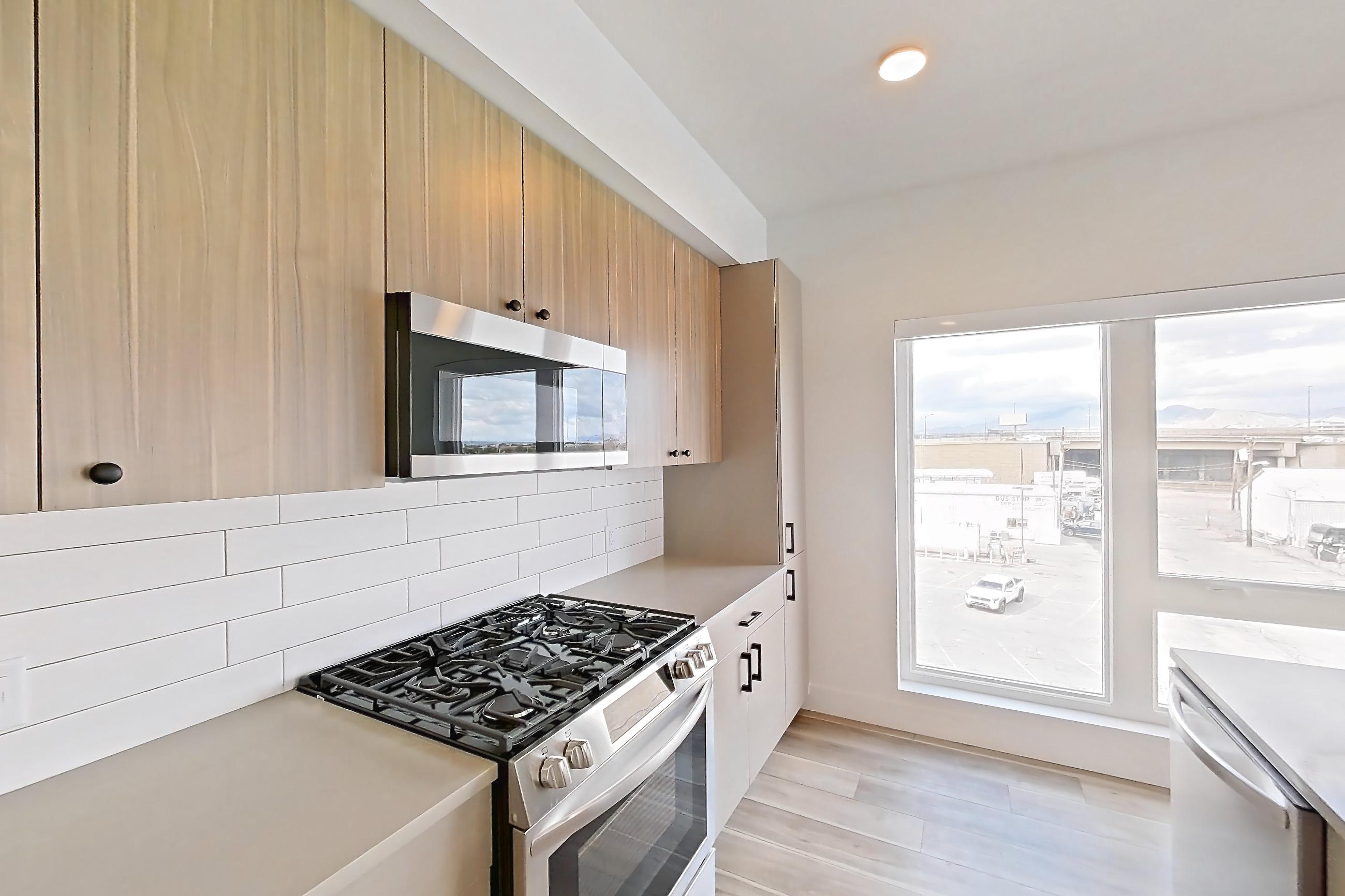 Kitchen with gas range, kitchen island, light countertops, light stone countertops, light wood-finish flooring, microwave, oven/range, refrigerator, and stainless steel appliances, Apartment 449 at The Myles