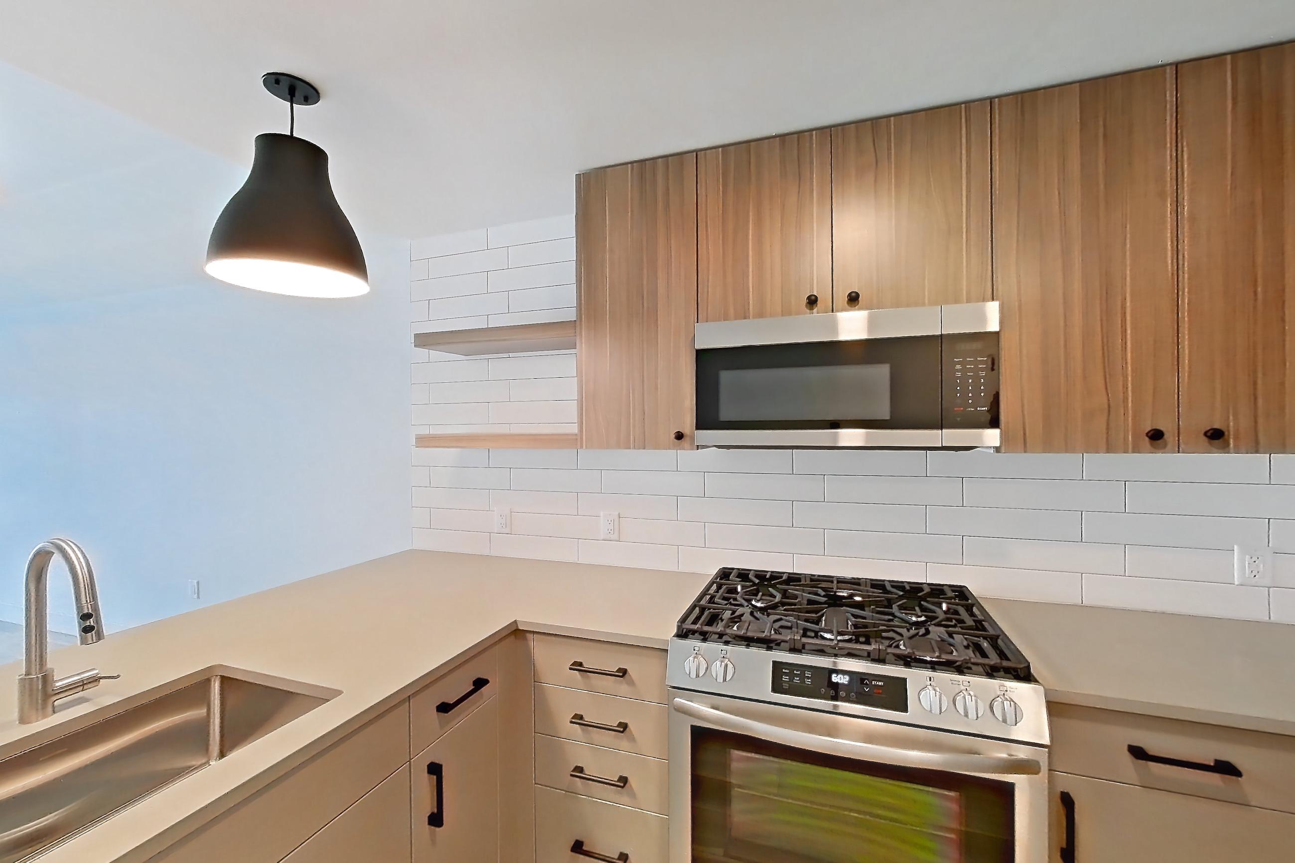 Kitchen with dishwasher, gas range, light countertops, light wood-finish flooring, microwave, oven/range, refrigerator, and stainless steel appliances, Apartment 450 at The Myles
