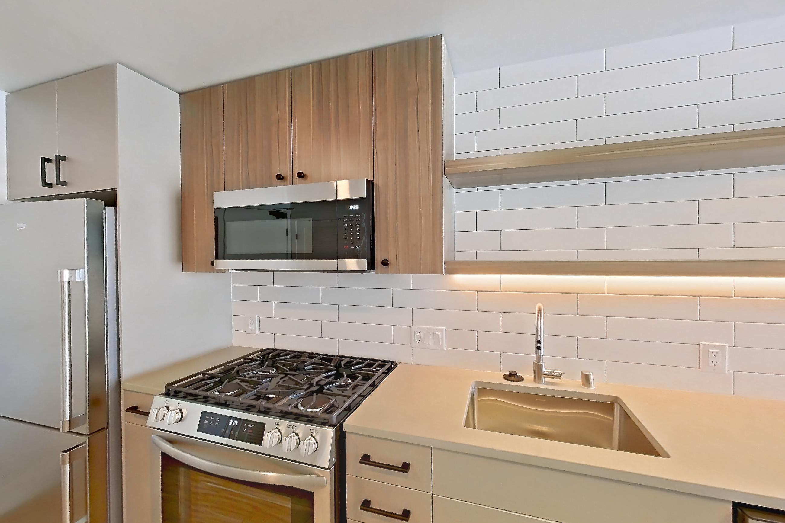 Kitchen with dishwasher, gas range, light countertops, light wood-finish flooring, microwave, oven/range, refrigerator, and stainless steel appliances, Apartment 509 at The Myles