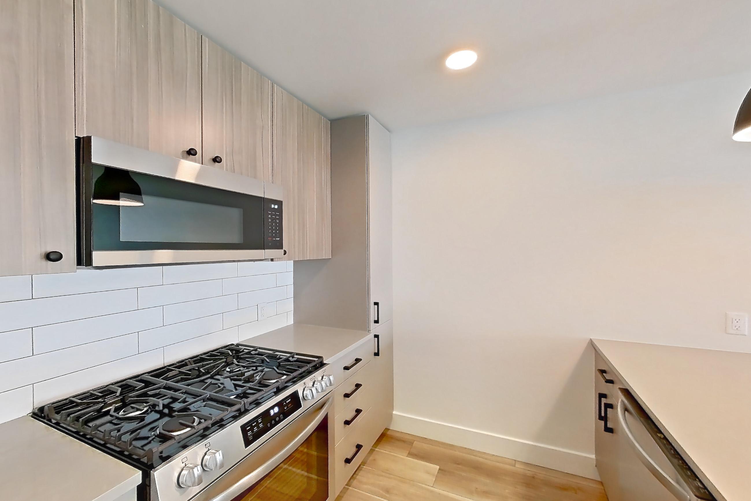 Kitchen with gas range, light countertops, light wood-finish flooring, oven/range, refrigerator, stainless steel appliances, and wood-look tile flooring, Apartment 511 at The Myles