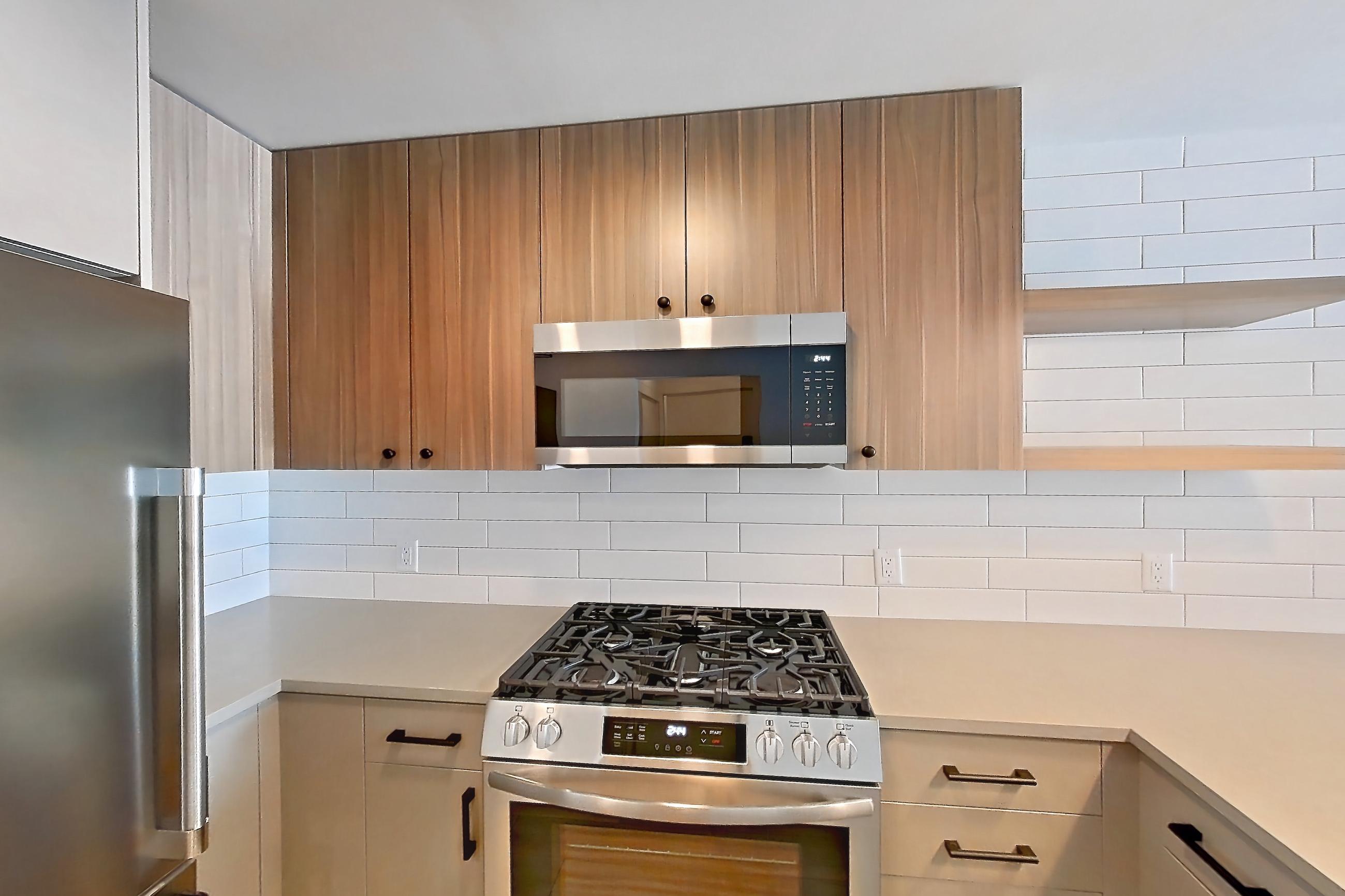 Kitchen with dishwasher, gas range, light countertops, light wood-finish flooring, microwave, oven/range, refrigerator, and stainless steel appliances, Apartment 512 at The Myles
