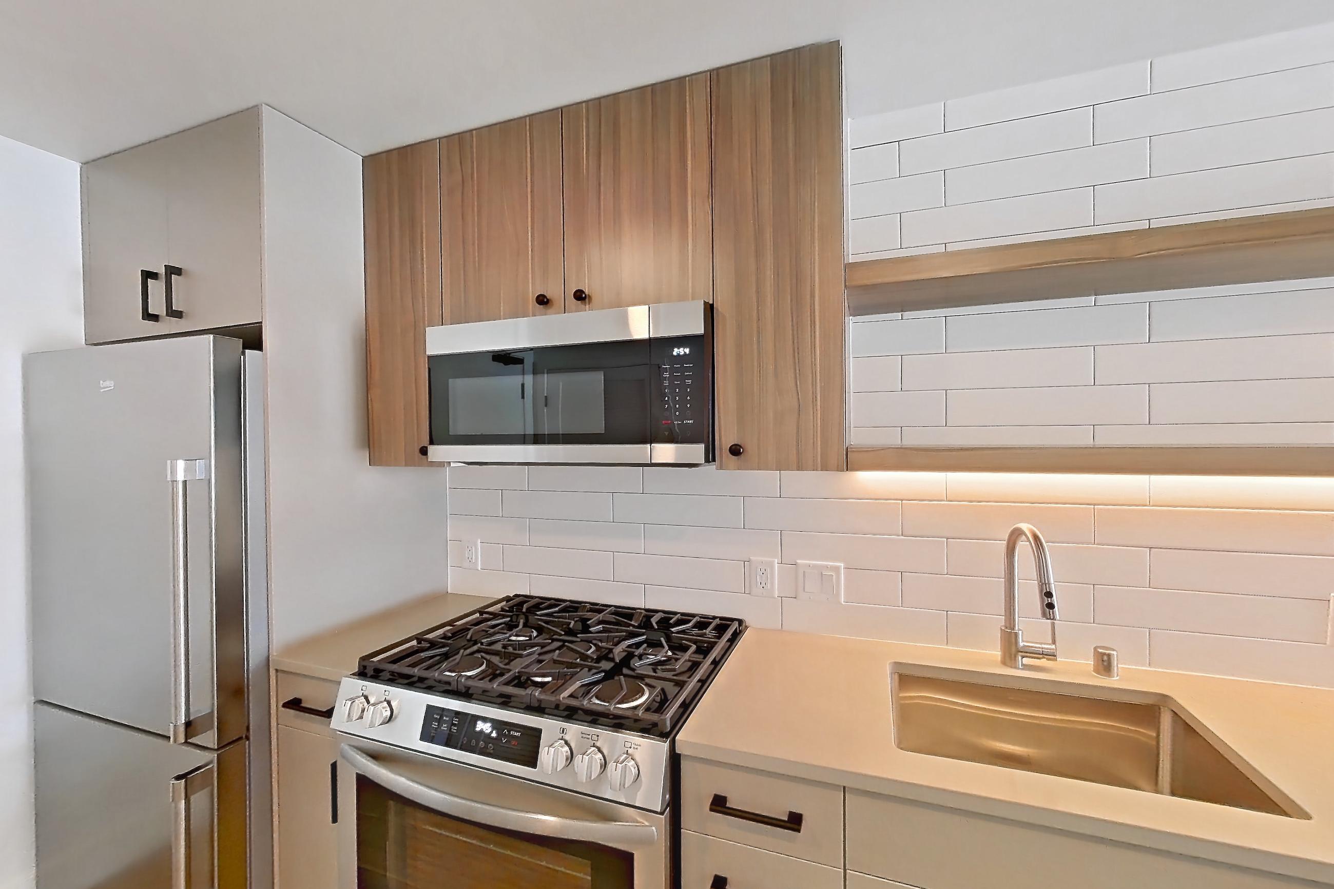 Kitchen with dishwasher, gas range, light countertops, light wood-finish flooring, microwave, oven/range, refrigerator, and stainless steel appliances, Apartment 516 at The Myles
