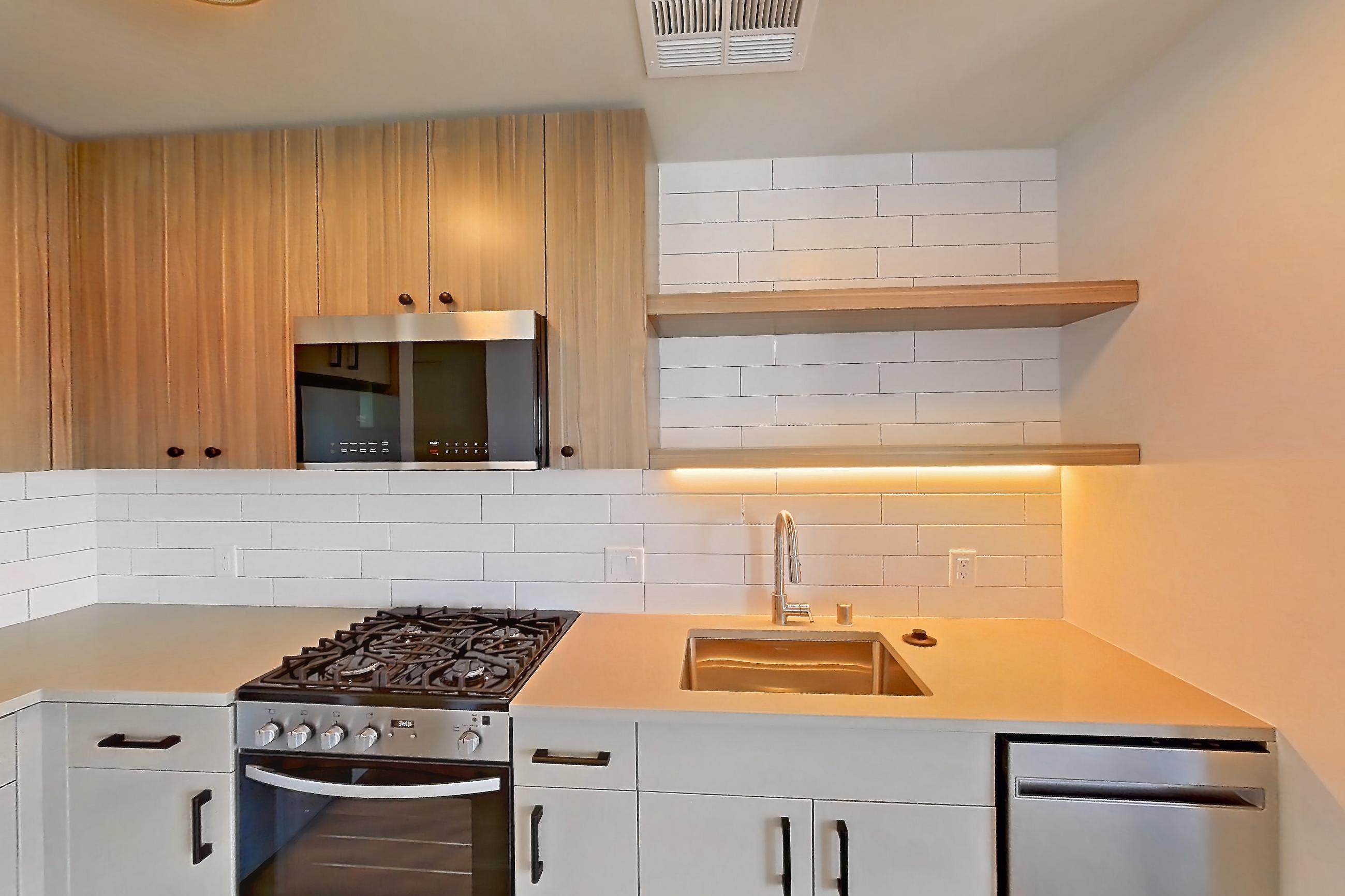 Kitchen with dishwasher, gas range, light countertops, light wood-finish flooring, oven/range, refrigerator, and stainless steel appliances, Apartment 518 at The Myles