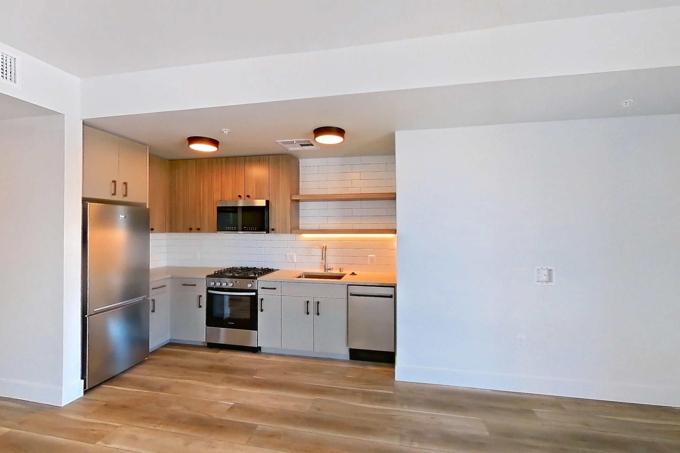 Living space with dishwasher, gas range, light countertops, light wood-finish flooring, oven/range, stainless steel appliances, and wood-look tile flooring, Apartment 518 at The Myles