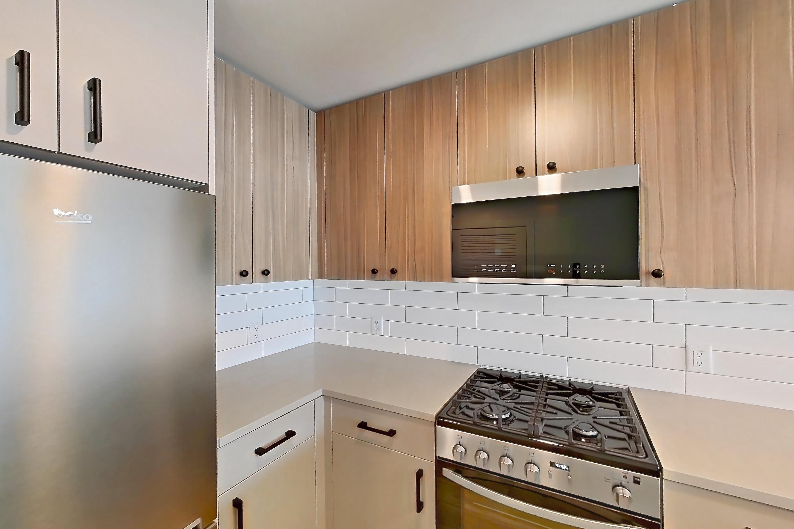 Kitchen with dishwasher, gas range, light countertops, light wood-finish flooring, oven/range, refrigerator, and stainless steel appliances, Apartment 519 at The Myles
