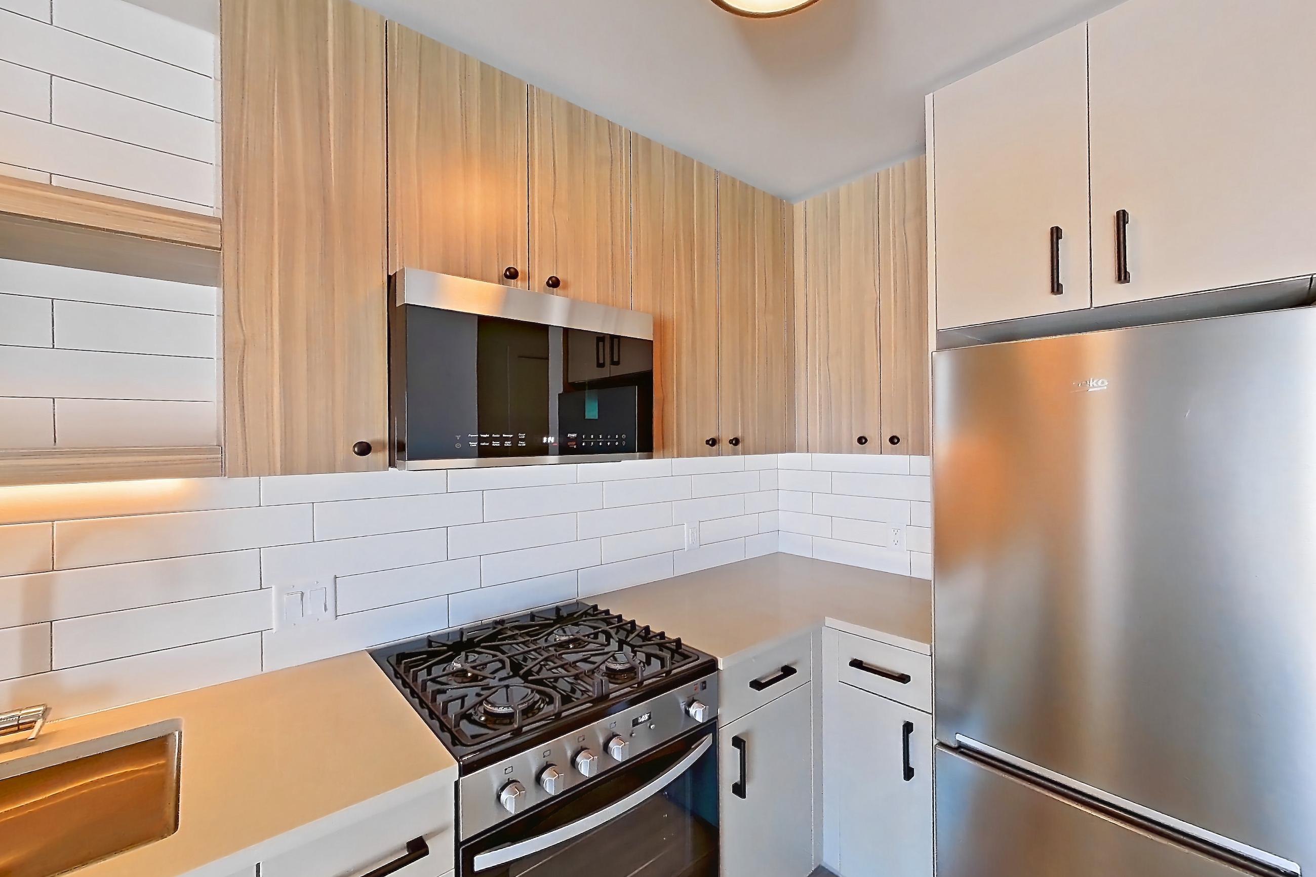 Kitchen with dishwasher, gas range, light countertops, light wood-finish flooring, oven/range, refrigerator, and stainless steel appliances, Apartment 520 at The Myles