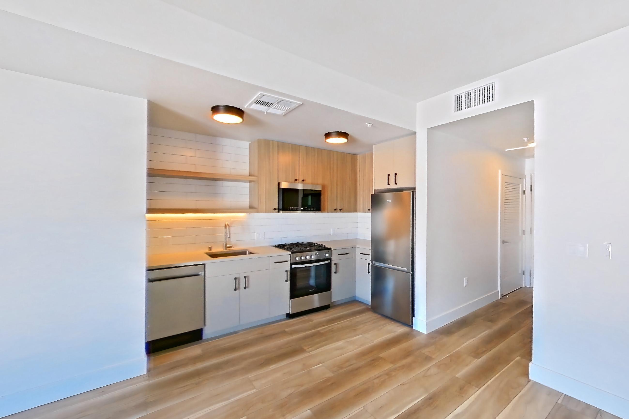 Living space with dishwasher, gas range, light countertops, light wood-finish flooring, oven/range, refrigerator, and stainless steel appliances, Apartment 520 at The Myles