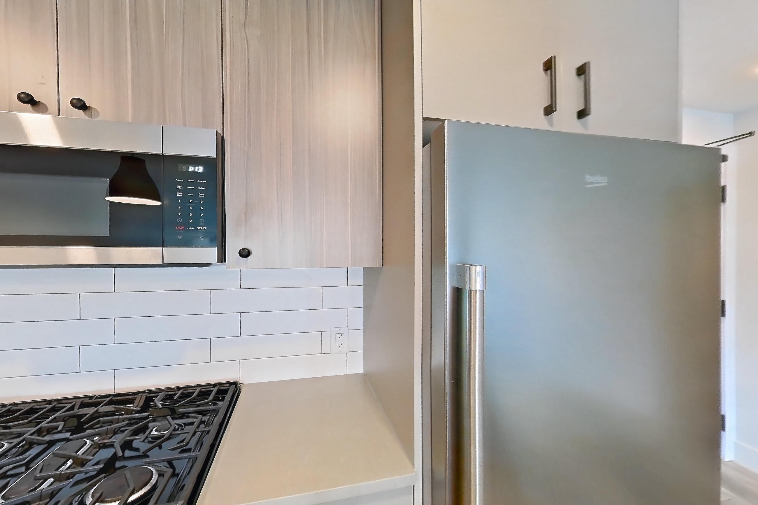 Kitchen with dishwasher, gas range, light countertops, light wood-finish flooring, microwave, oven/range, refrigerator, and stainless steel appliances, Apartment 521 at The Myles