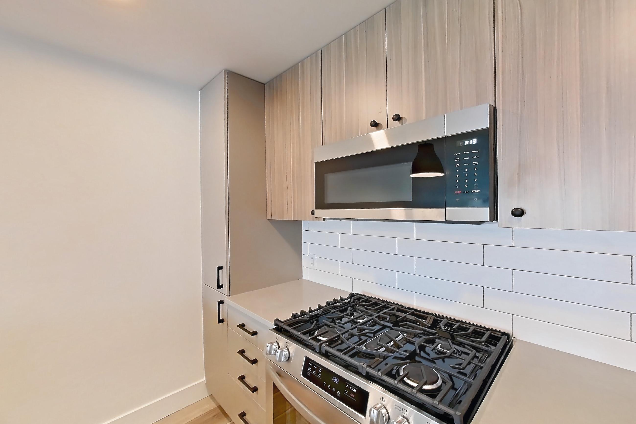 Kitchen with dishwasher, gas range, light countertops, light wood-finish flooring, microwave, oven/range, refrigerator, and stainless steel appliances, Apartment 521 at The Myles