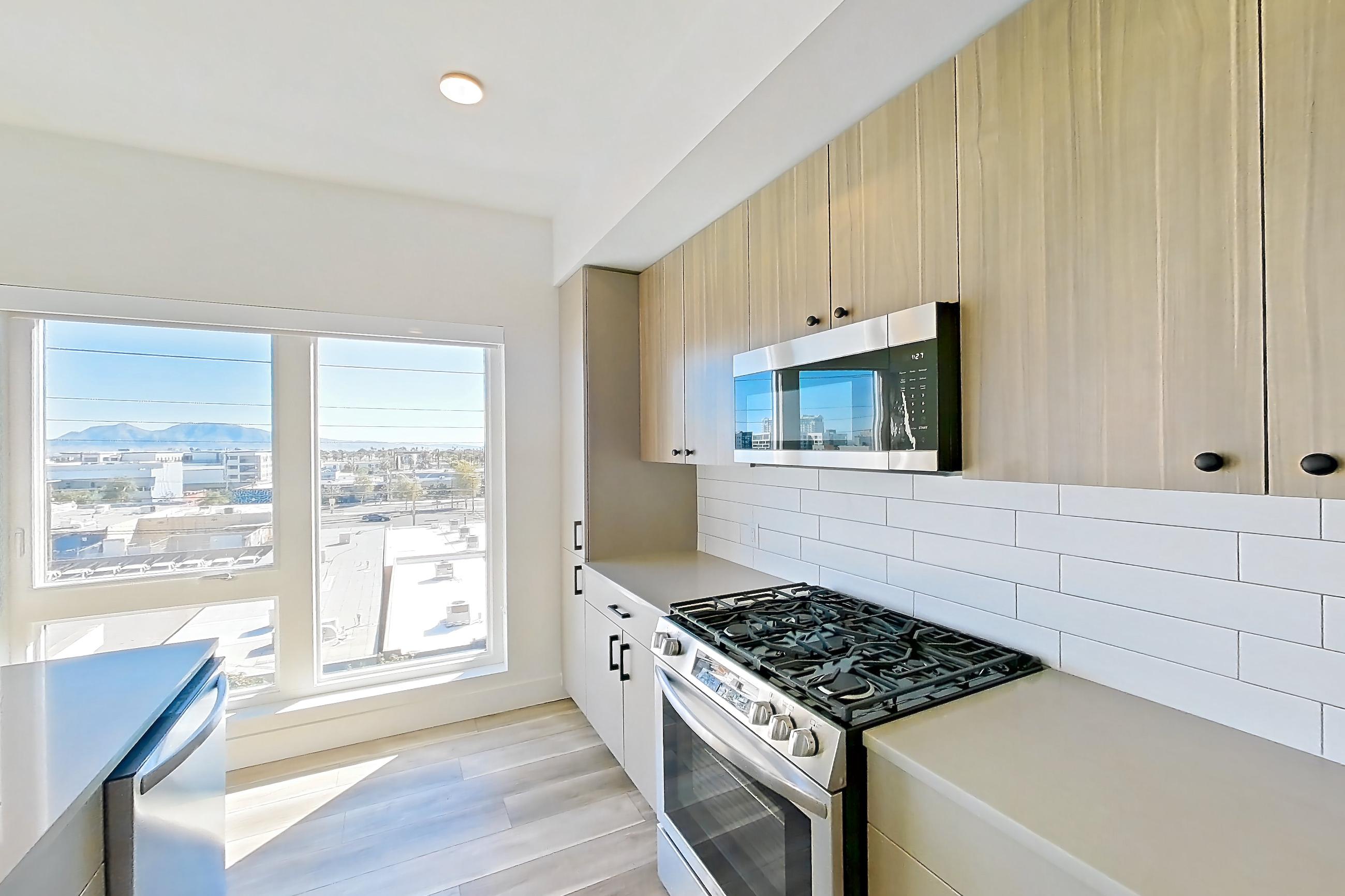 Kitchen with gas range, kitchen island, light countertops, light wood-finish flooring, microwave, oven/range, stainless steel appliances, and wood-look tile flooring, Apartment 524 at The Myles