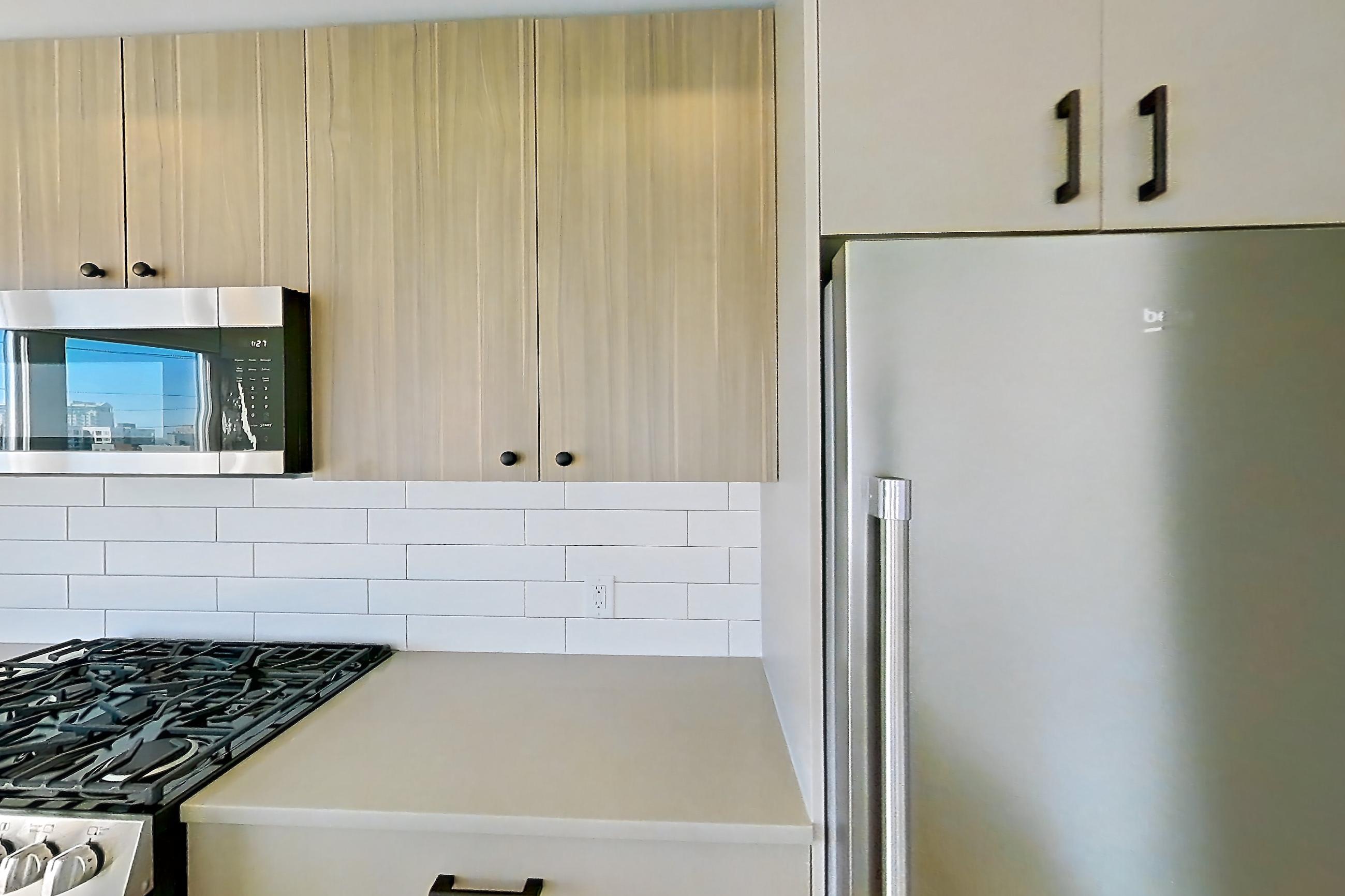 Kitchen with gas range, kitchen island, light countertops, light wood-finish flooring, microwave, oven/range, stainless steel appliances, and wood-look tile flooring, Apartment 524 at The Myles