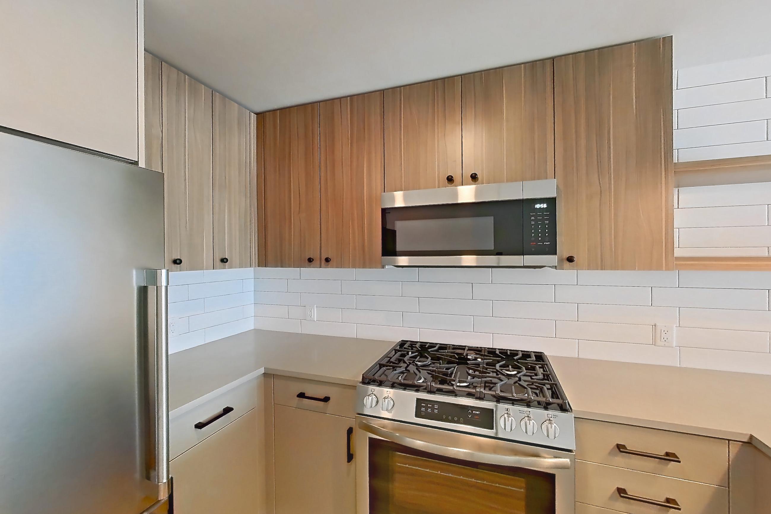 Kitchen with dishwasher, gas range, light countertops, light wood-finish flooring, microwave, oven/range, refrigerator, and stainless steel appliances, Apartment 525 at The Myles