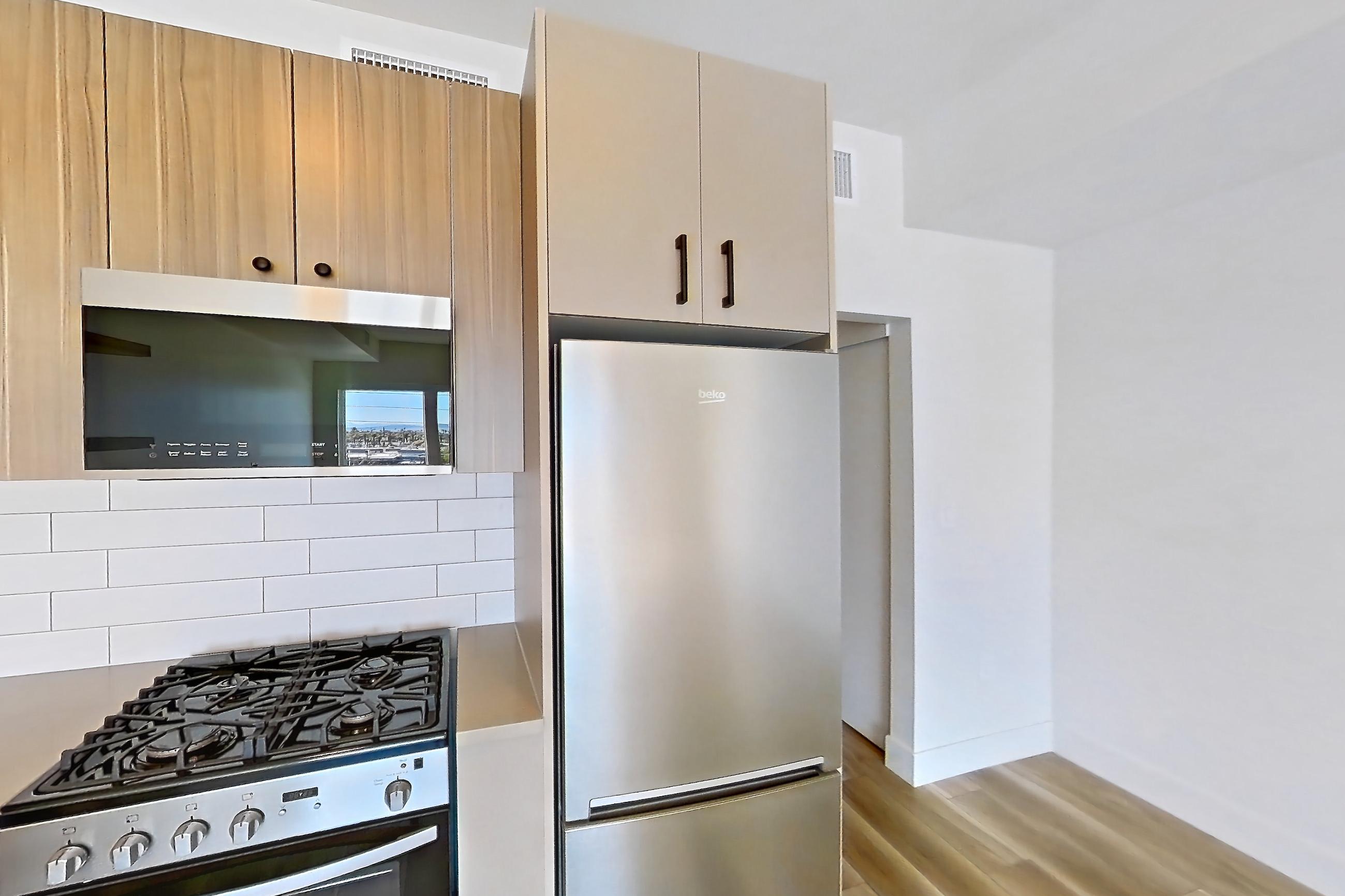Kitchen with dishwasher, gas range, light countertops, light wood-finish flooring, oven/range, refrigerator, and stainless steel appliances, Apartment 526 at The Myles
