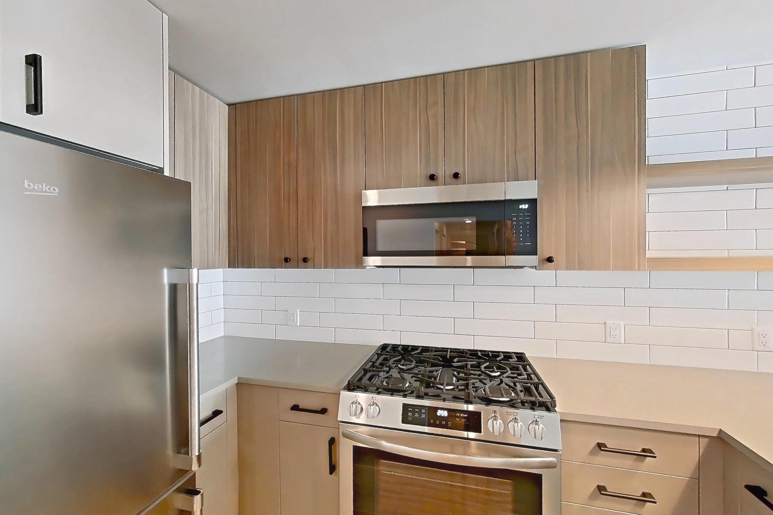 Kitchen with dishwasher, gas range, light countertops, light wood-finish flooring, oven/range, refrigerator, and stainless steel appliances, Apartment 527 at The Myles
