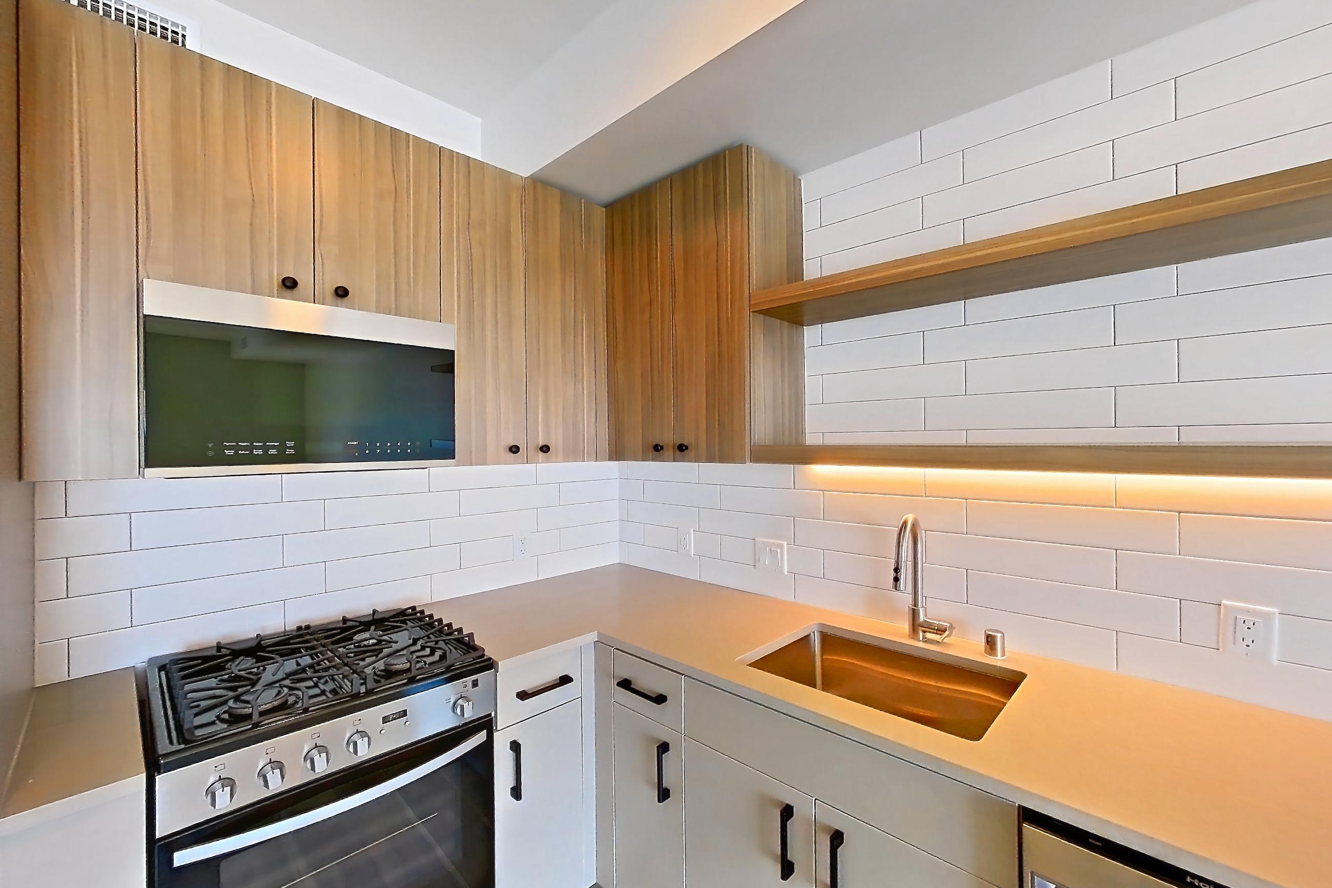 Kitchen with dishwasher, gas range, light countertops, light wood-finish flooring, oven/range, refrigerator, and stainless steel appliances, Apartment 528 at The Myles