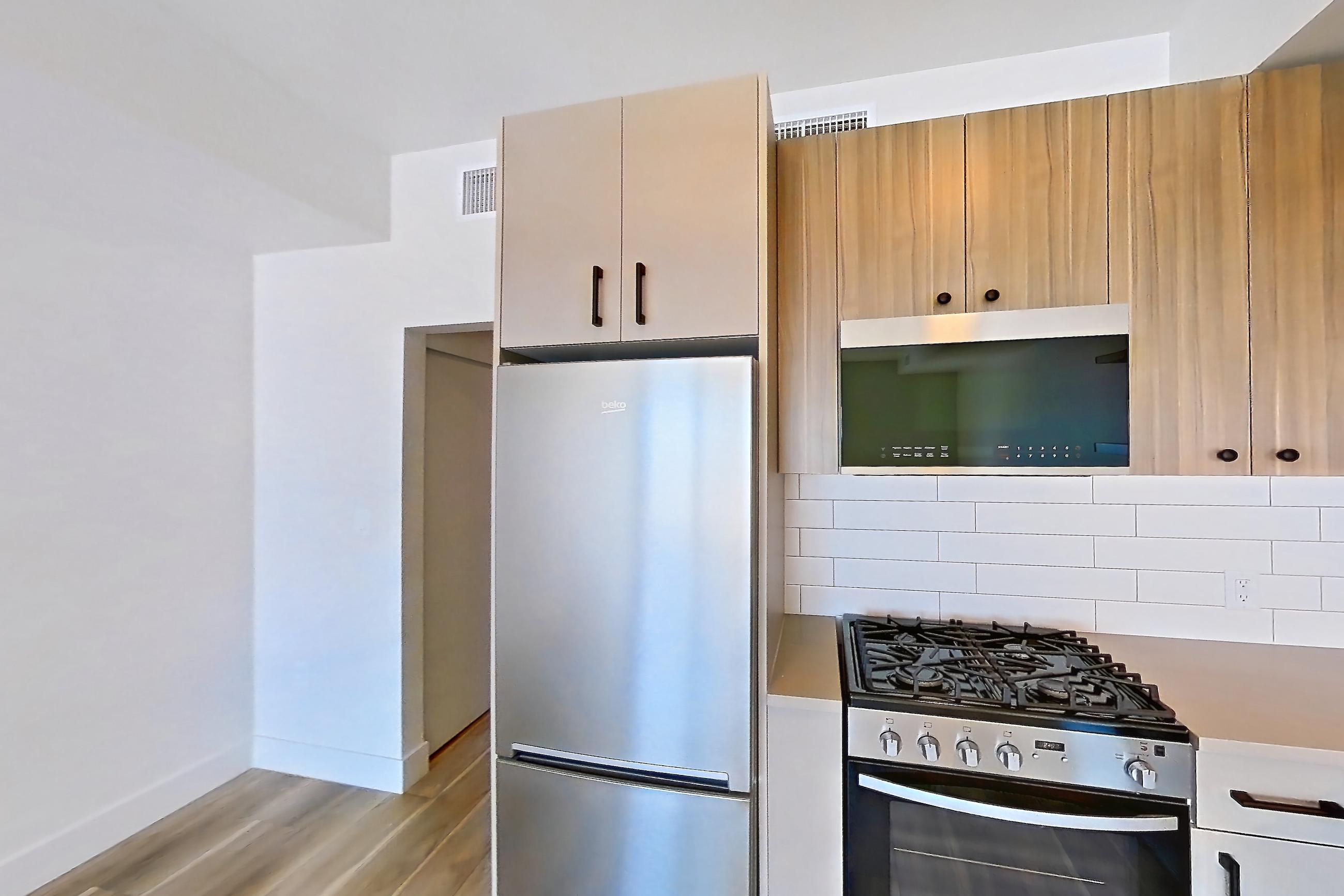Kitchen with dishwasher, gas range, light countertops, light wood-finish flooring, oven/range, refrigerator, and stainless steel appliances, Apartment 528 at The Myles