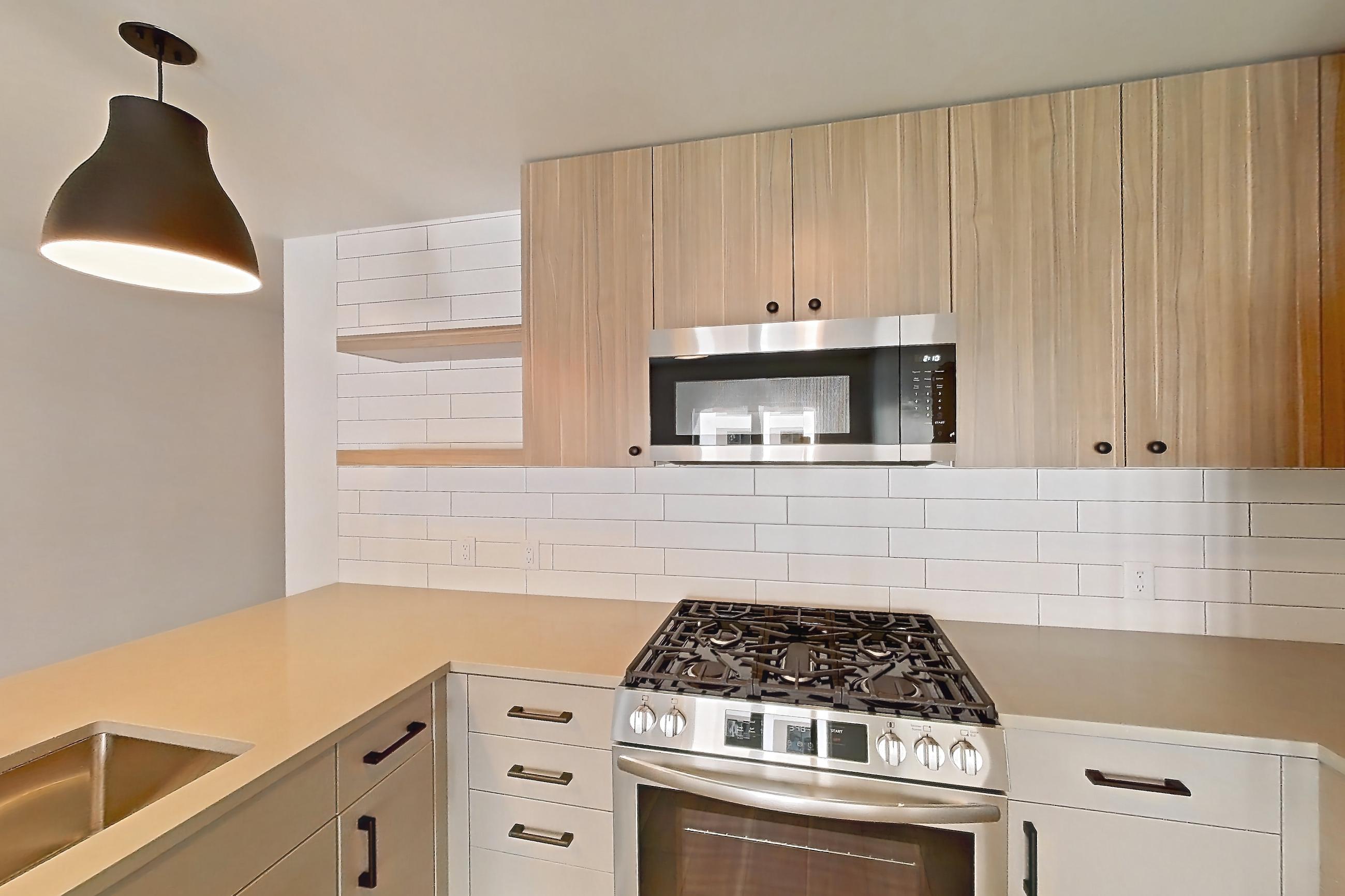 Kitchen with dishwasher, gas range, light countertops, light wood-finish flooring, microwave, oven/range, refrigerator, and stainless steel appliances, Apartment 529 at The Myles