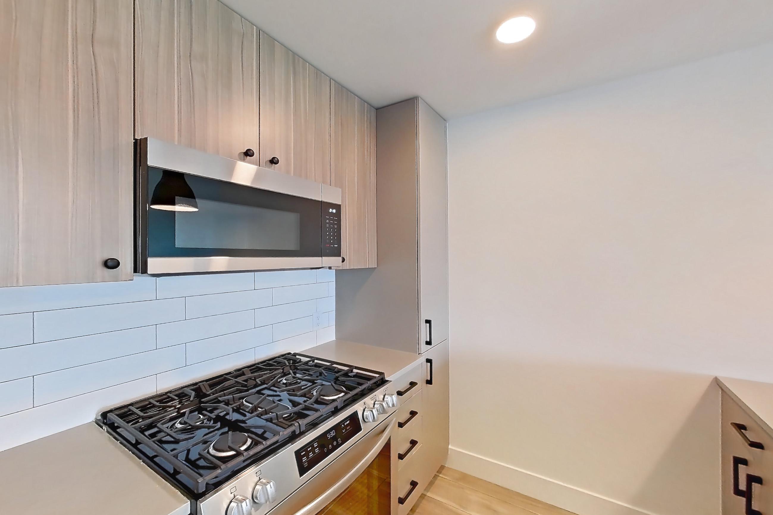 Kitchen with dishwasher, gas range, light countertops, light wood-finish flooring, microwave, oven/range, and stainless steel appliances, Apartment 530 at The Myles