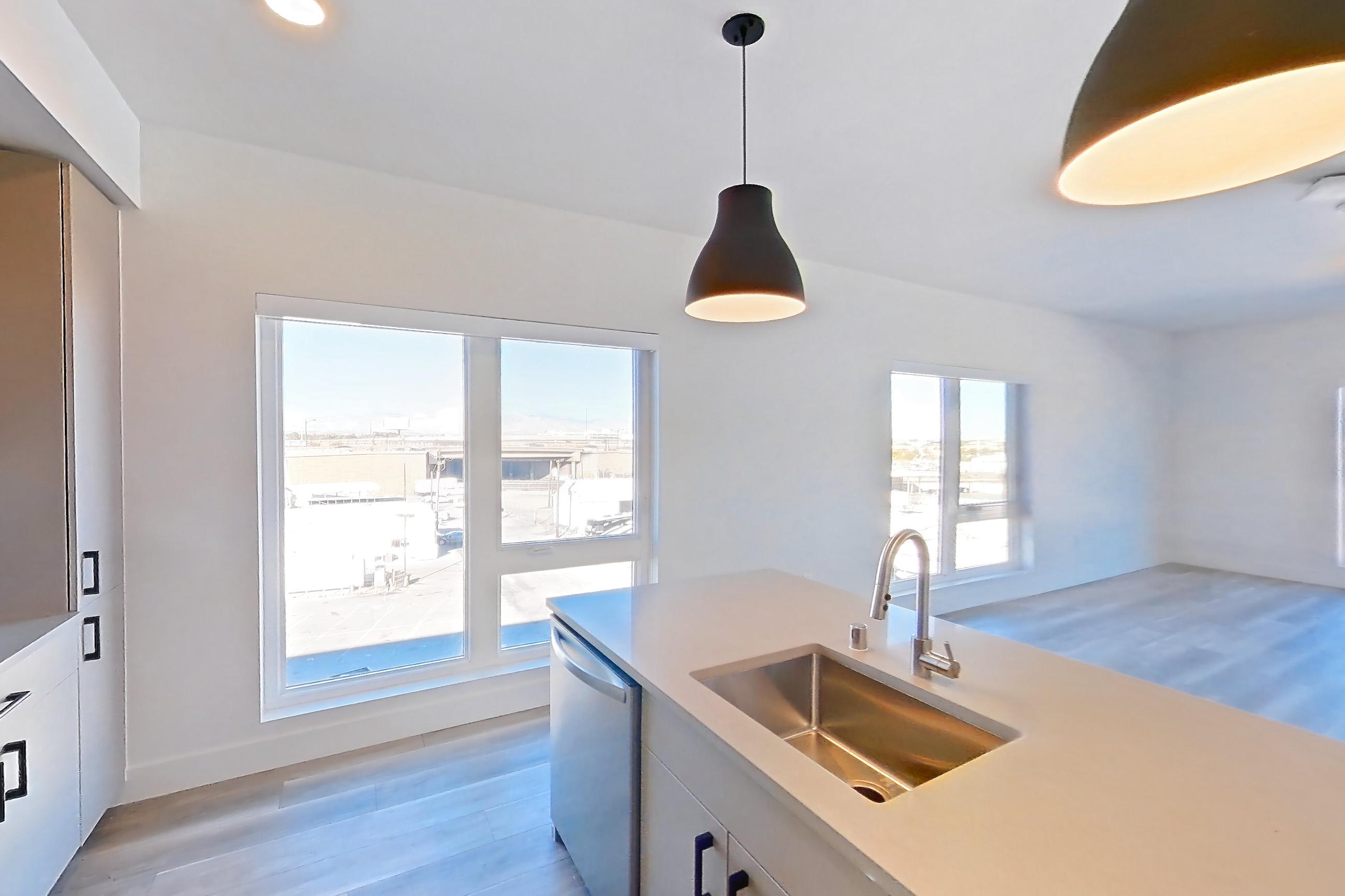 Kitchen with dishwasher, gas range, kitchen island, light countertops, light stone countertops, light wood-finish flooring, oven/range, refrigerator, and stainless steel appliances, Apartment 549 at The Myles