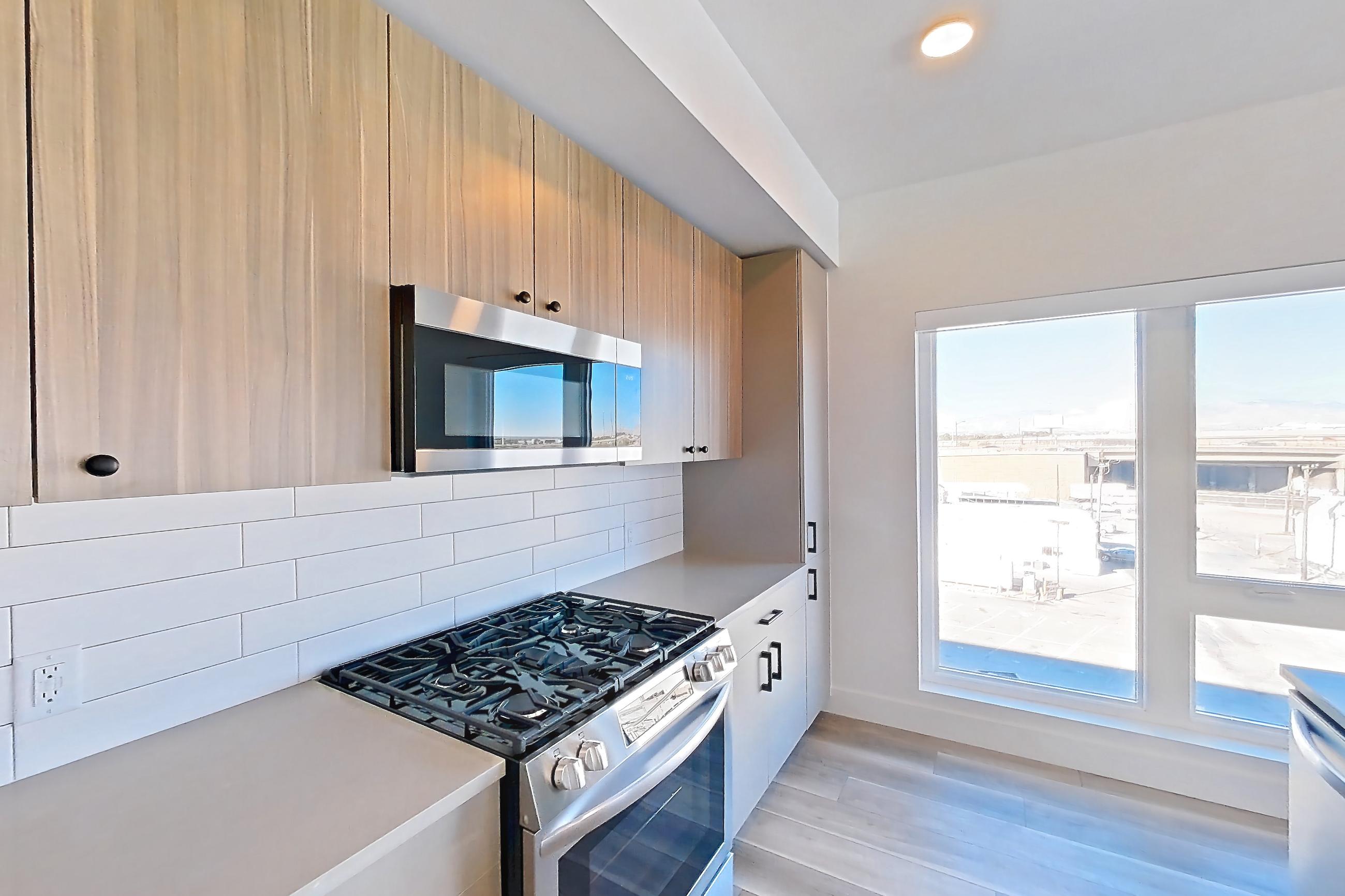 Kitchen with dishwasher, gas range, kitchen island, light countertops, light stone countertops, light wood-finish flooring, oven/range, refrigerator, and stainless steel appliances, Apartment 549 at The Myles