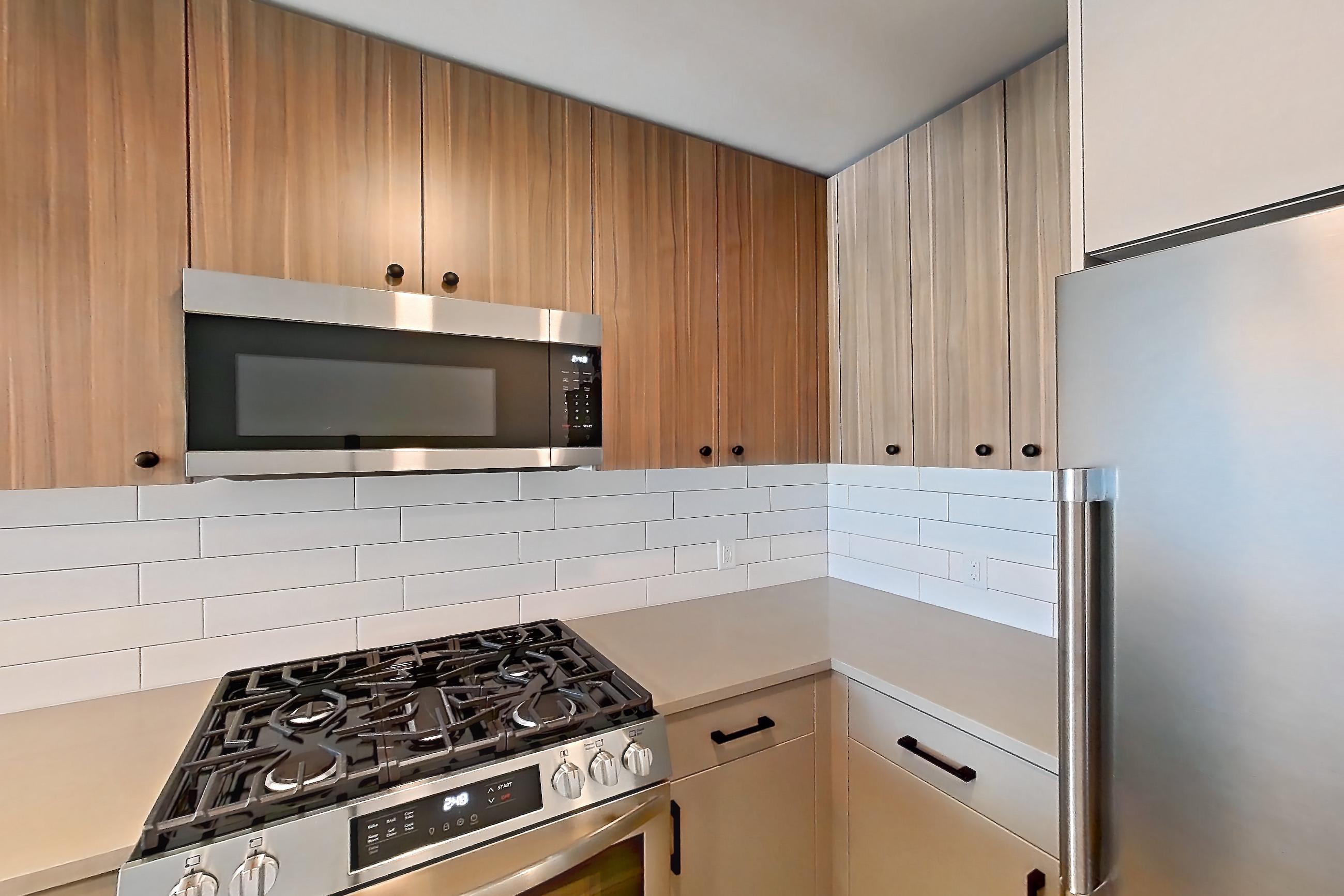 Kitchen with dishwasher, gas range, light countertops, light wood-finish flooring, microwave, oven/range, refrigerator, and stainless steel appliances, Apartment 550 at The Myles