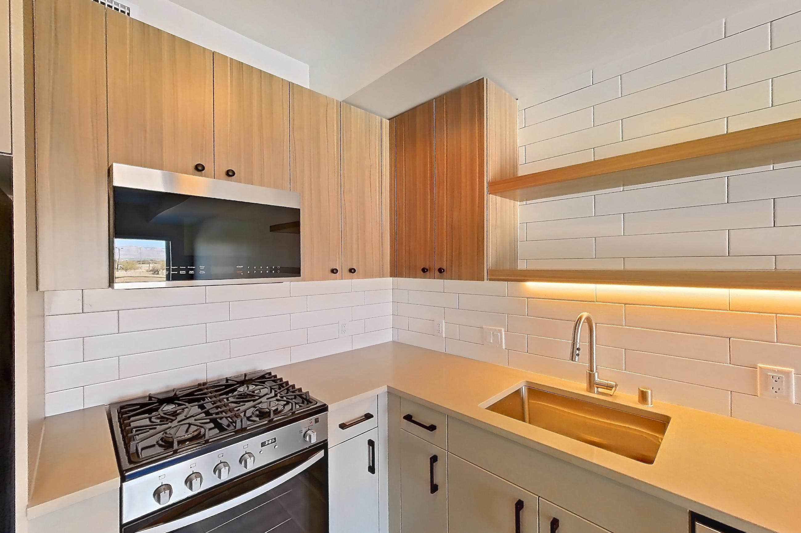 Kitchen with dishwasher, gas range, light countertops, light stone countertops, light wood-finish flooring, oven/range, refrigerator, and stainless steel appliances, Apartment 551 at The Myles