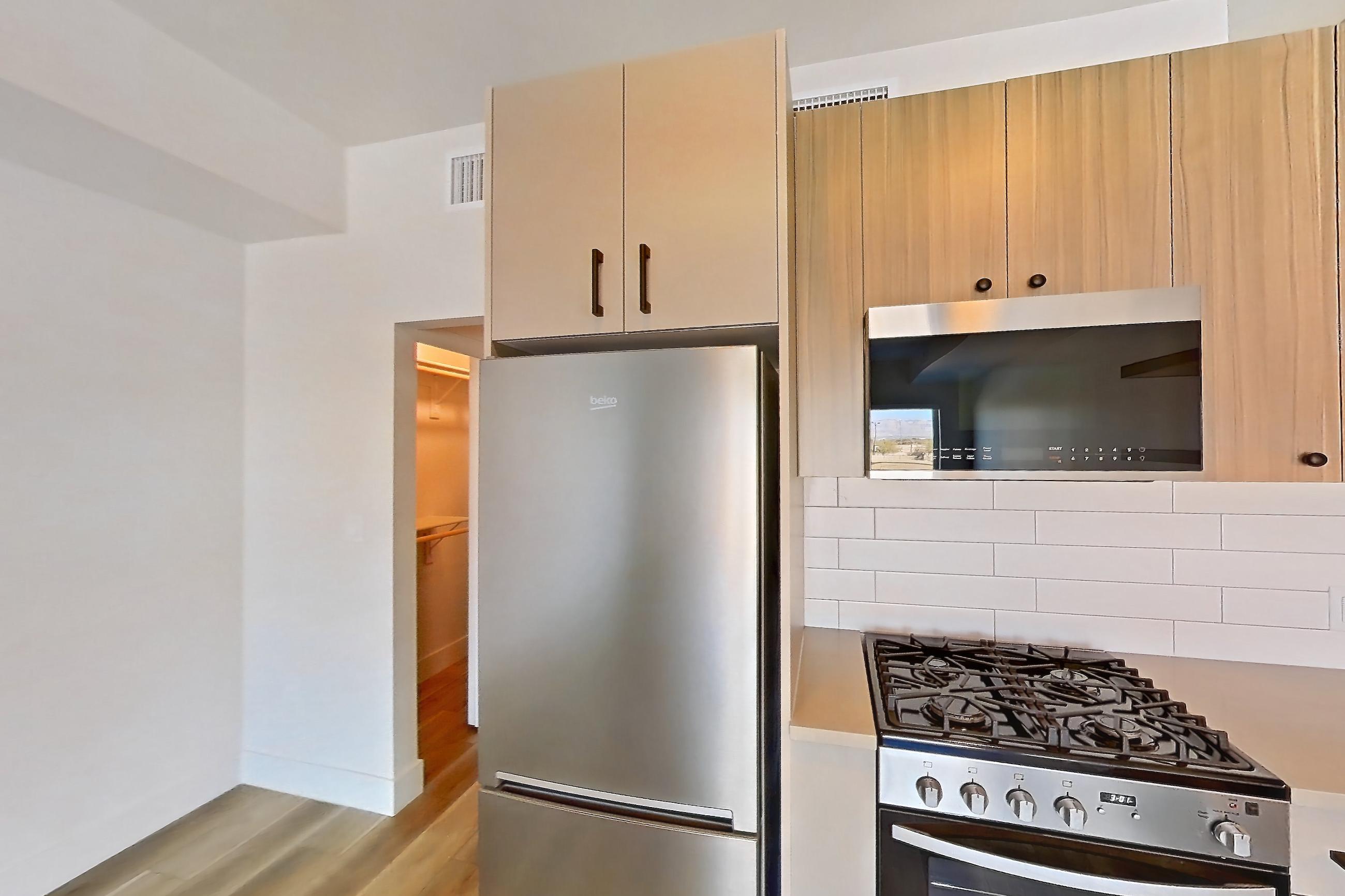 Kitchen with dishwasher, gas range, light countertops, light stone countertops, light wood-finish flooring, oven/range, refrigerator, and stainless steel appliances, Apartment 551 at The Myles
