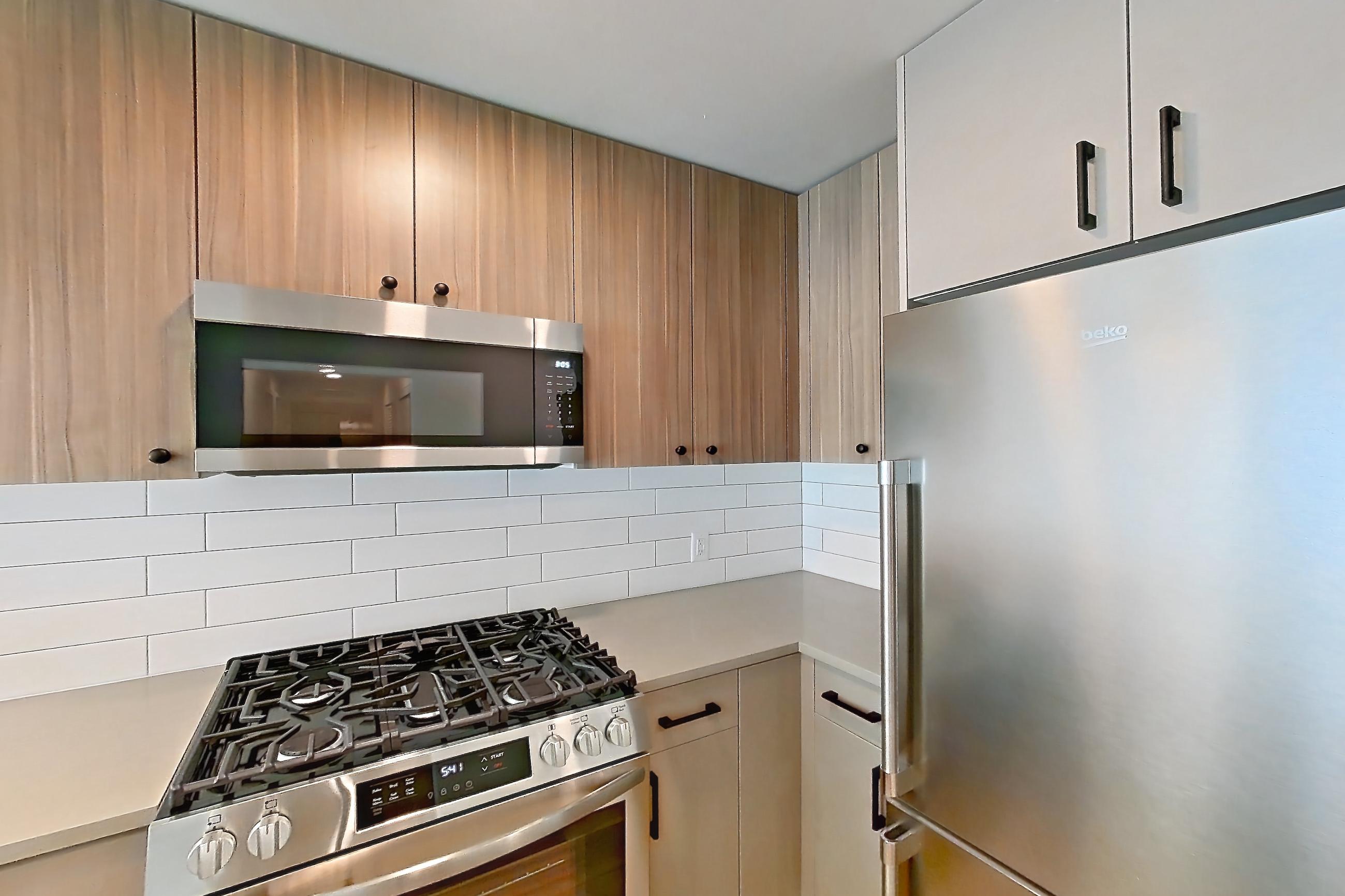 Kitchen with dishwasher, gas range, light countertops, light wood-finish flooring, microwave, oven/range, refrigerator, and stainless steel appliances, Apartment 552 at The Myles