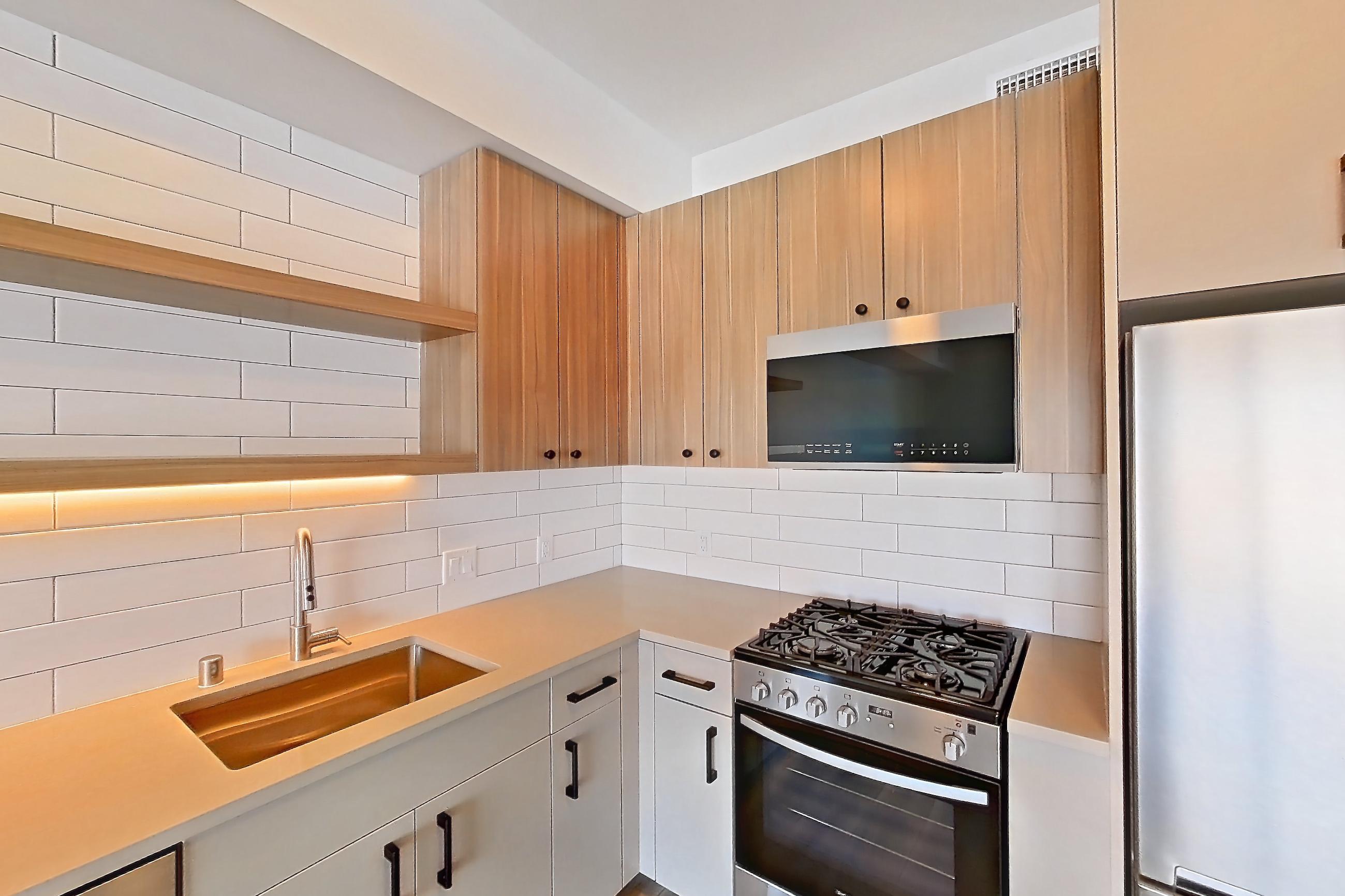 Kitchen with dishwasher, gas range, light countertops, light wood-finish flooring, oven/range, refrigerator, and stainless steel appliances, Apartment 553 at The Myles