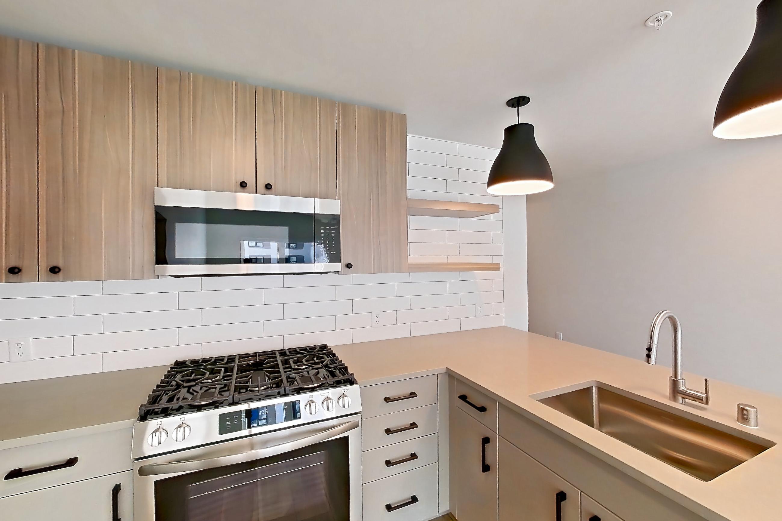 Kitchen with dishwasher, gas range, light countertops, light wood-finish flooring, microwave, oven/range, refrigerator, and stainless steel appliances, Apartment 554 at The Myles