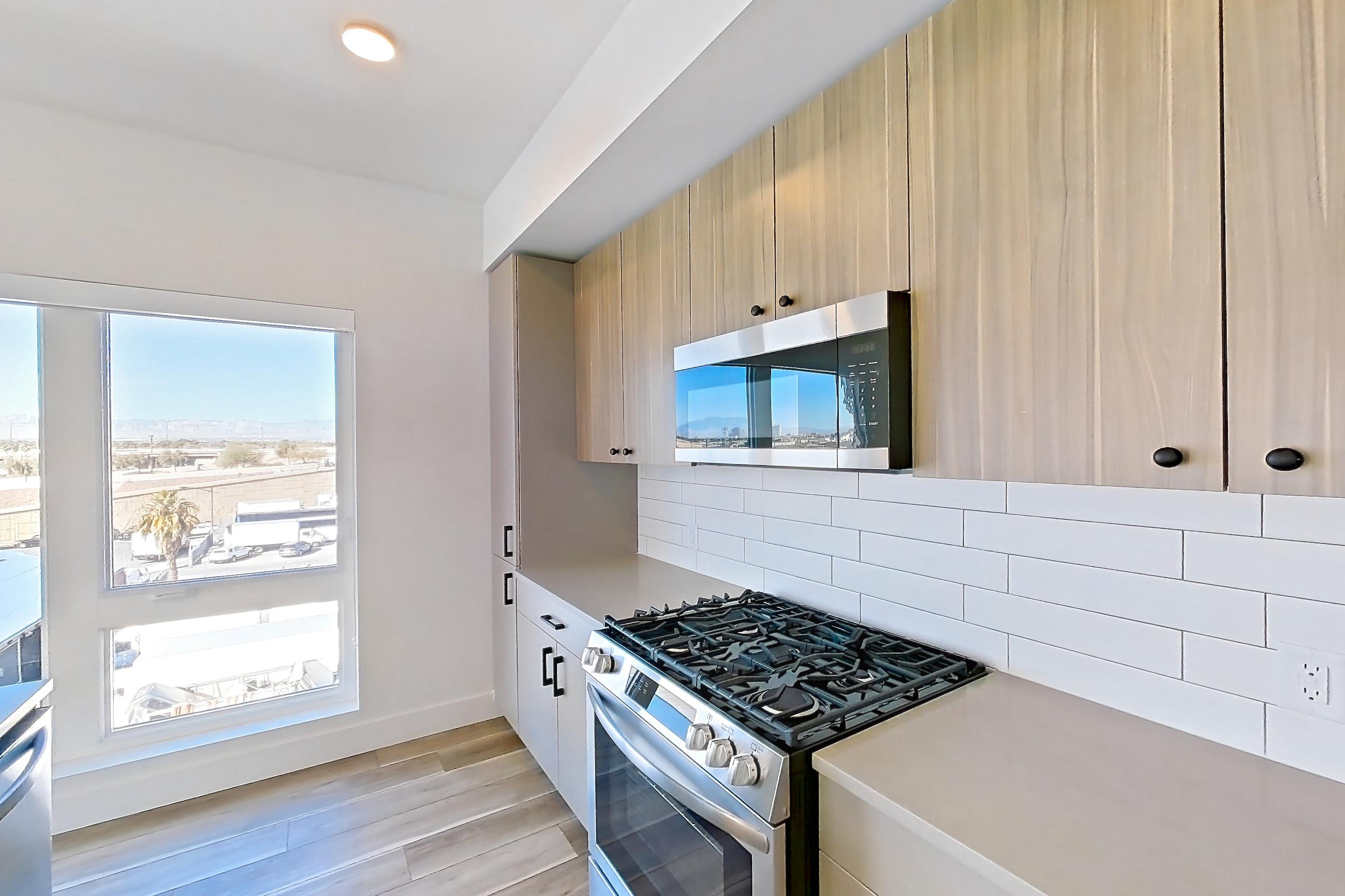Kitchen with dishwasher, gas range, kitchen island, light countertops, light stone countertops, light wood-finish flooring, microwave, oven/range, refrigerator, stainless steel appliances, and wood-look tile flooring, Apartment 556 at The Myles
