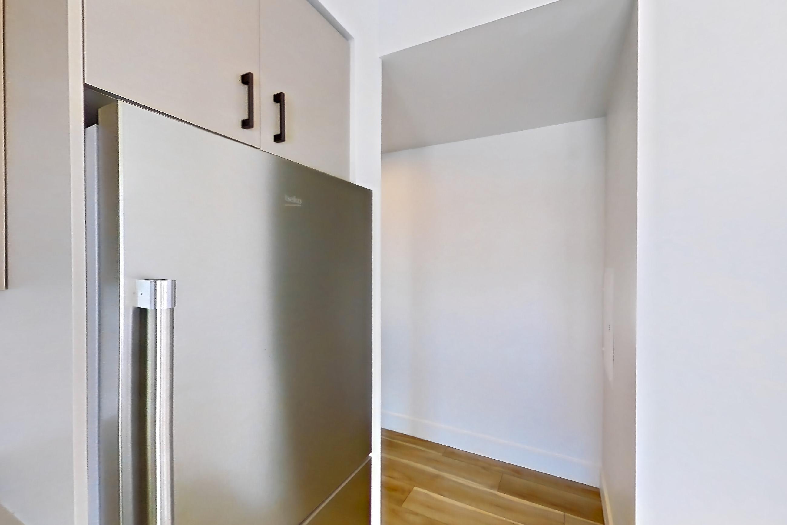Kitchen with dishwasher, gas range, kitchen island, light countertops, light stone countertops, light wood-finish flooring, microwave, oven/range, refrigerator, stainless steel appliances, and wood-look tile flooring, Apartment 556 at The Myles