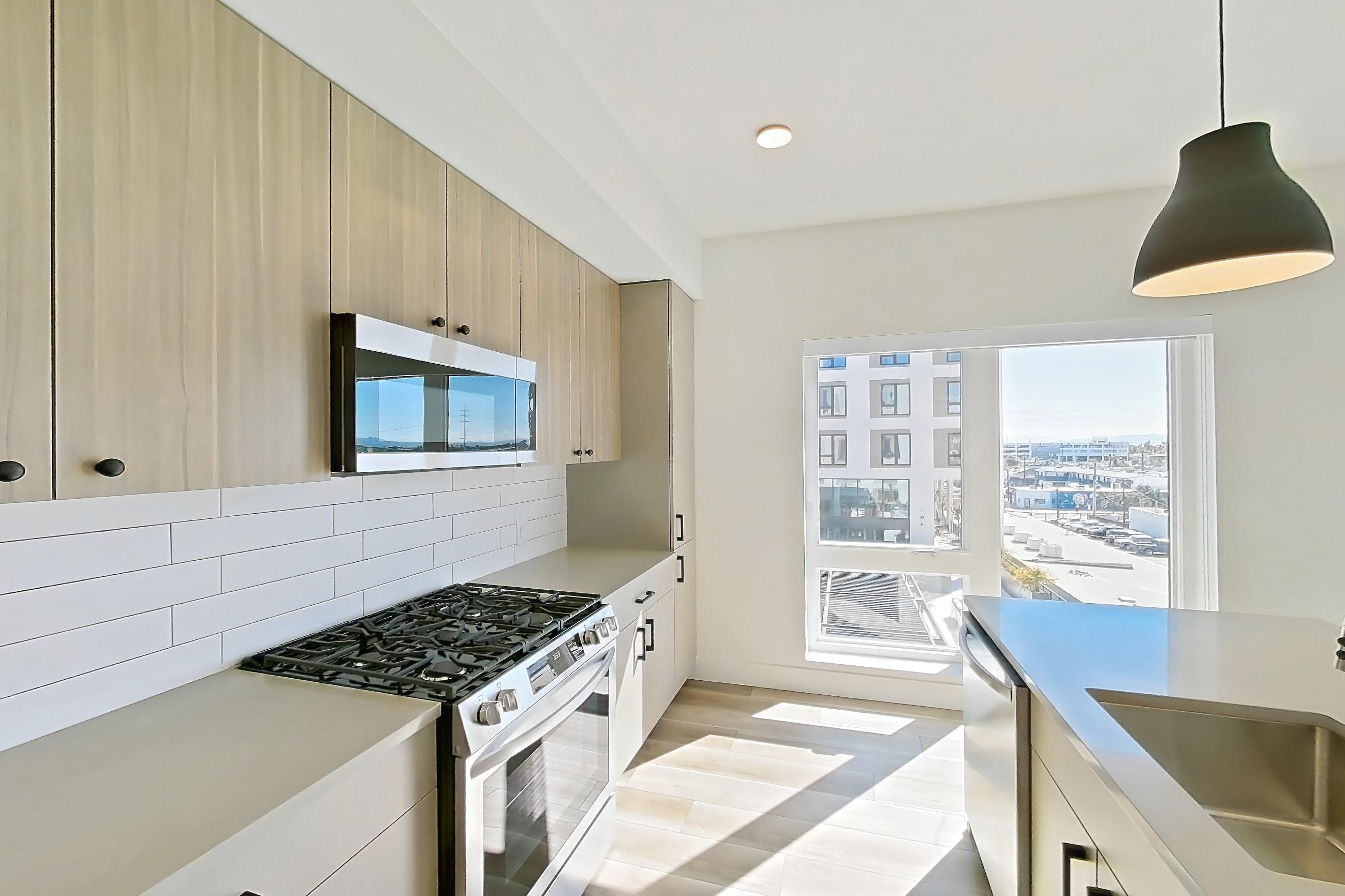Kitchen with gas range, kitchen island, light countertops, light wood-finish flooring, oven/range, stainless steel appliances, and wood-look tile flooring, Apartment 558 at The Myles