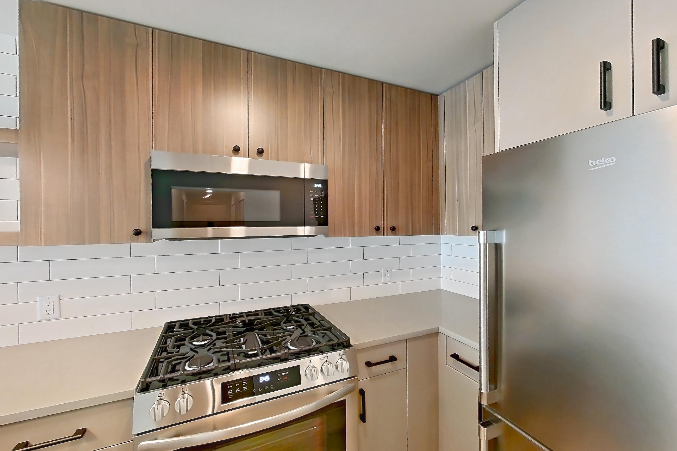 Kitchen with dishwasher, gas range, light countertops, light wood-finish flooring, microwave, oven/range, refrigerator, and stainless steel appliances, Apartment 601 at The Myles