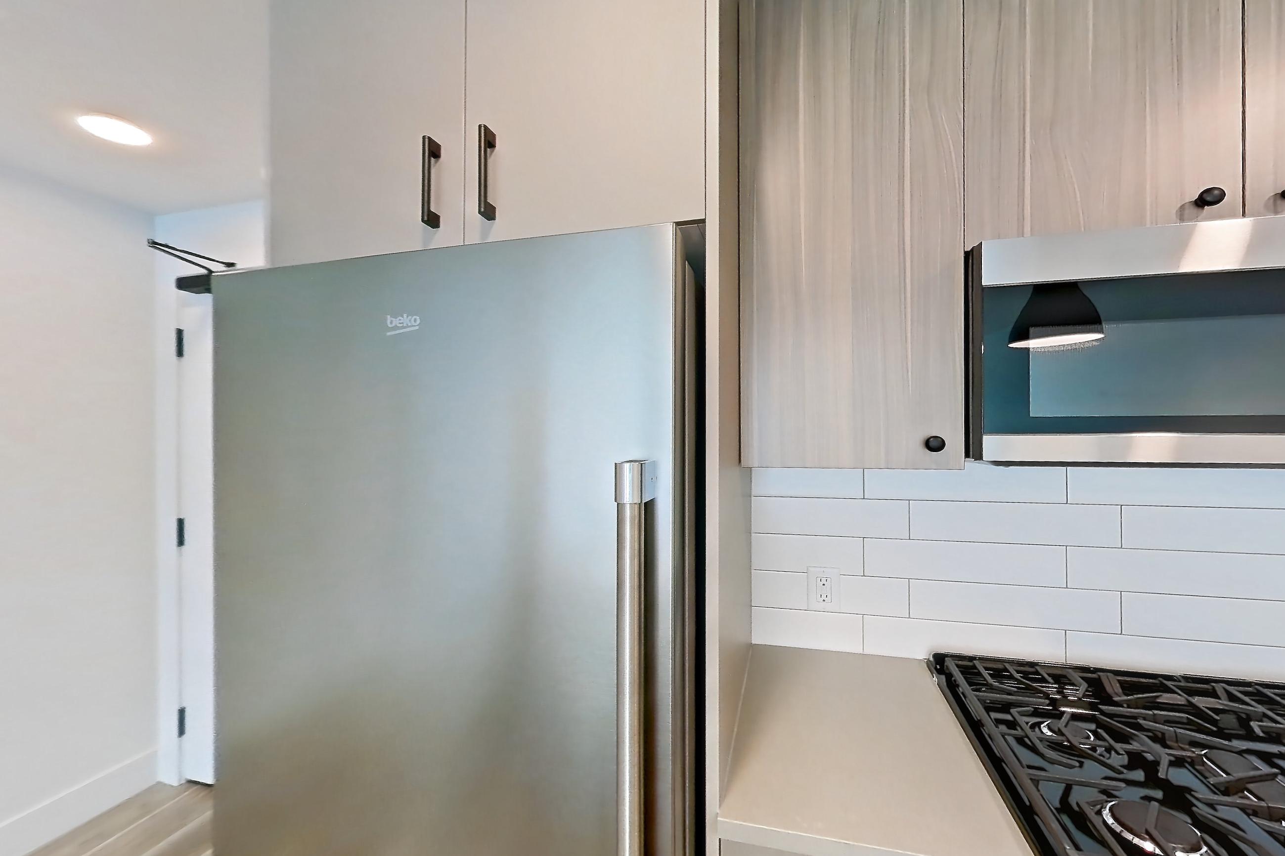Kitchen with dishwasher, gas range, light countertops, light wood-finish flooring, microwave, oven/range, and stainless steel appliances, Apartment 603 at The Myles