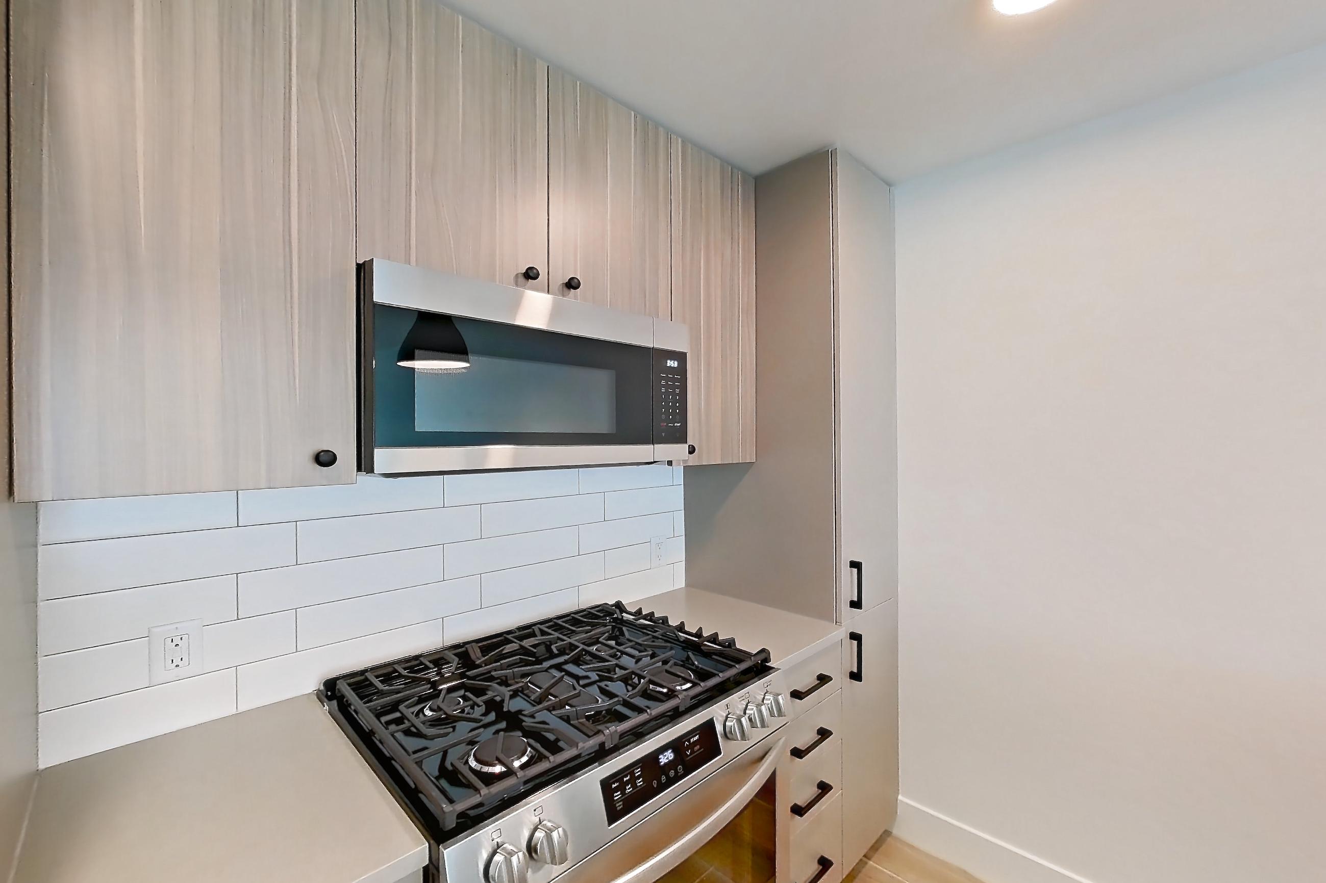 Kitchen with dishwasher, gas range, light countertops, light wood-finish flooring, microwave, oven/range, and stainless steel appliances, Apartment 603 at The Myles