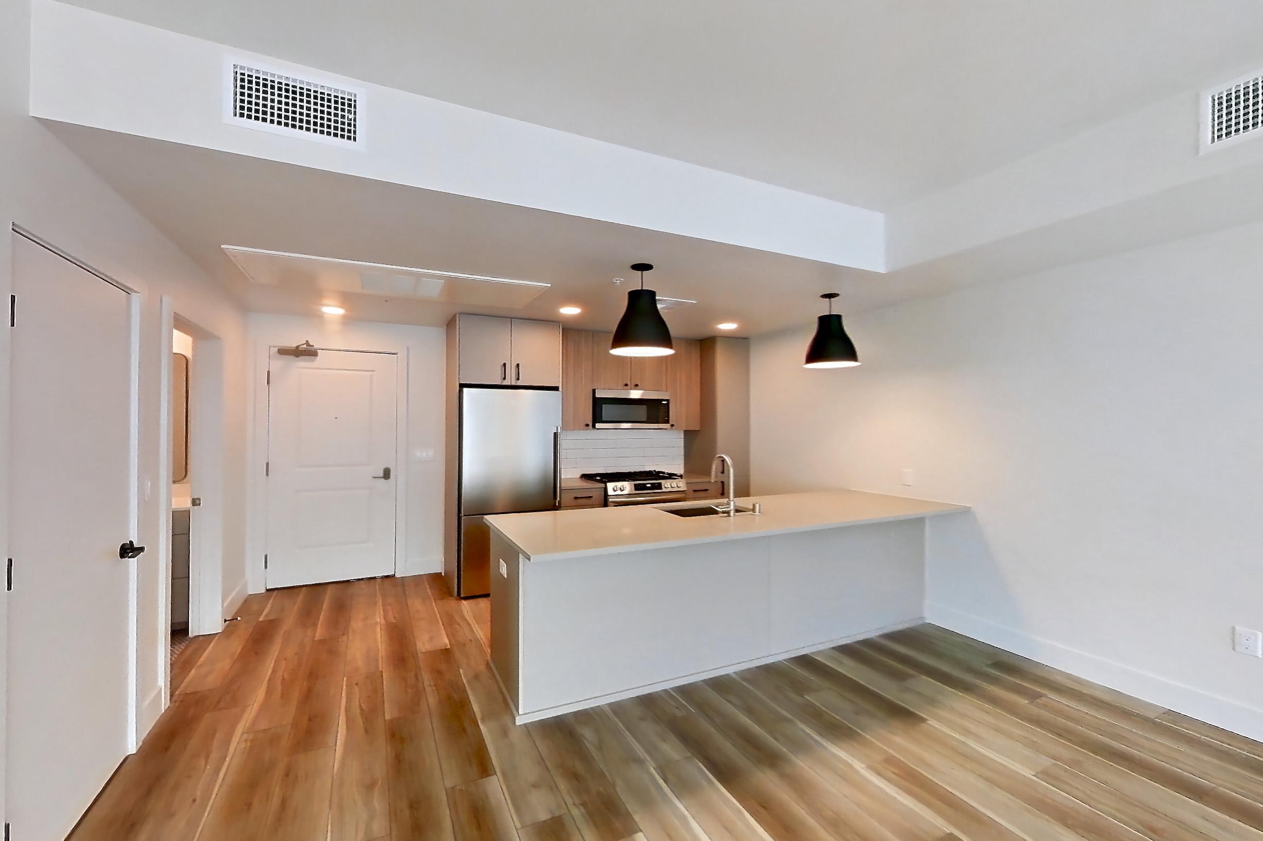 Living room with gas range, light countertops, light wood-finish flooring, oven/range, refrigerator, and stainless steel appliances, Apartment 603 at The Myles