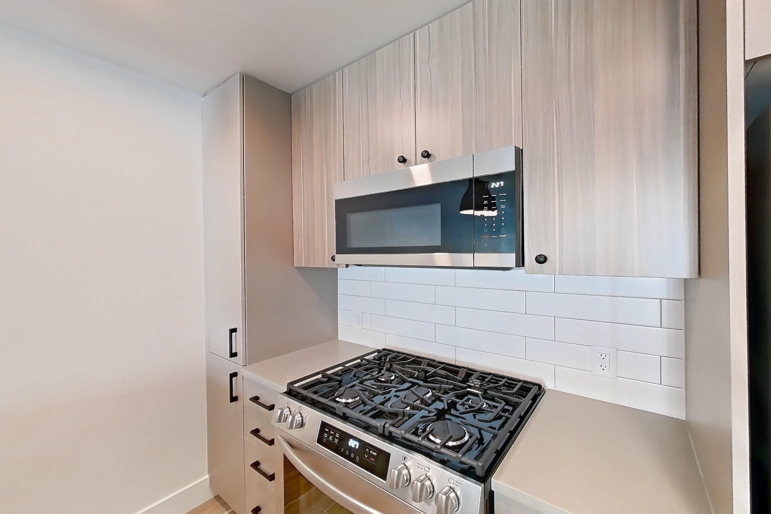 Kitchen with dishwasher, gas range, light countertops, light wood-finish flooring, microwave, oven/range, and stainless steel appliances, Apartment 604 at The Myles