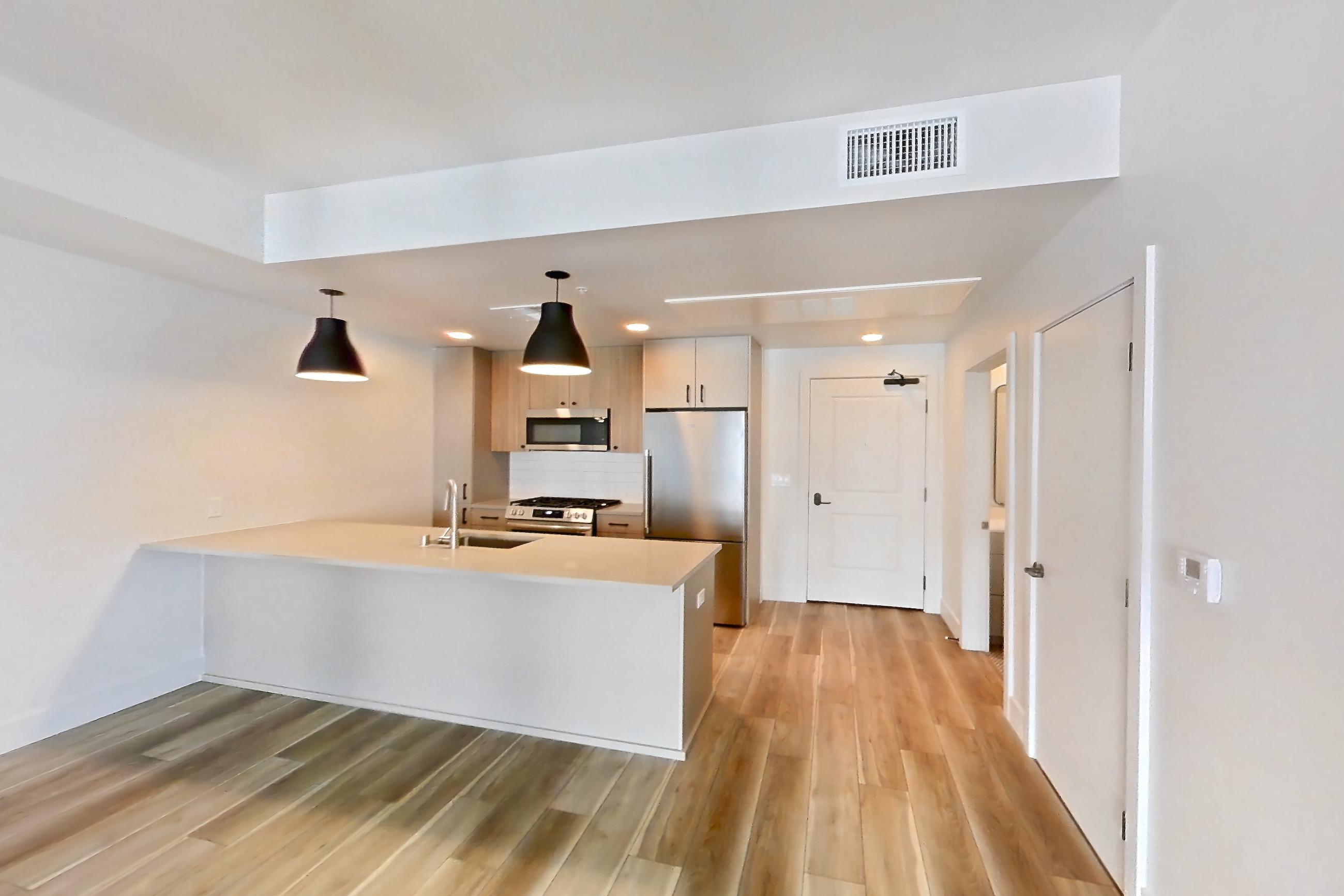 Living room with gas range, light countertops, light wood-finish flooring, refrigerator, and stainless steel appliances, Apartment 604 at The Myles