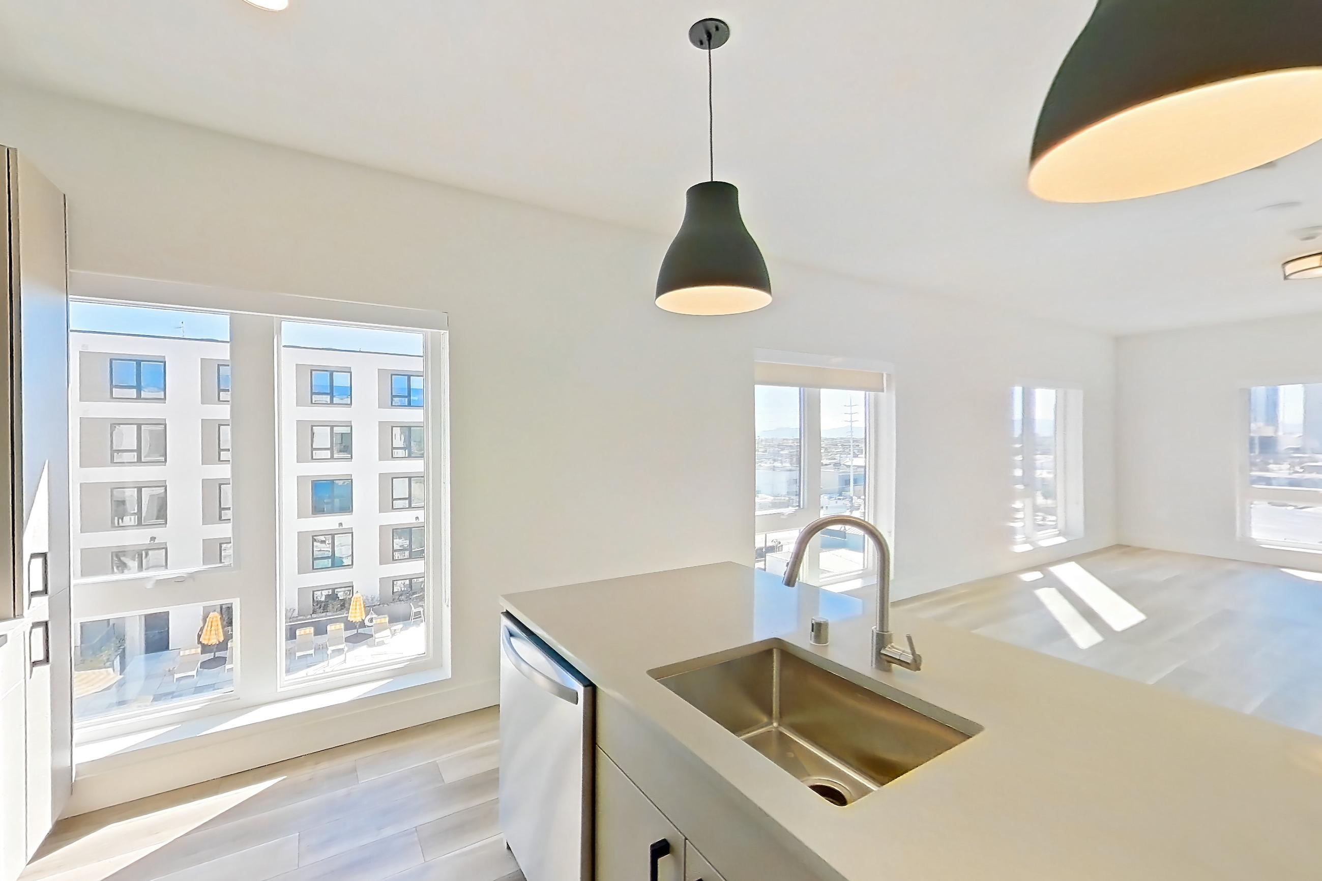 Kitchen with dishwasher, gas range, kitchen island, light countertops, light stone countertops, light wood-finish flooring, microwave, oven/range, and stainless steel appliances, Apartment 605 at The Myles