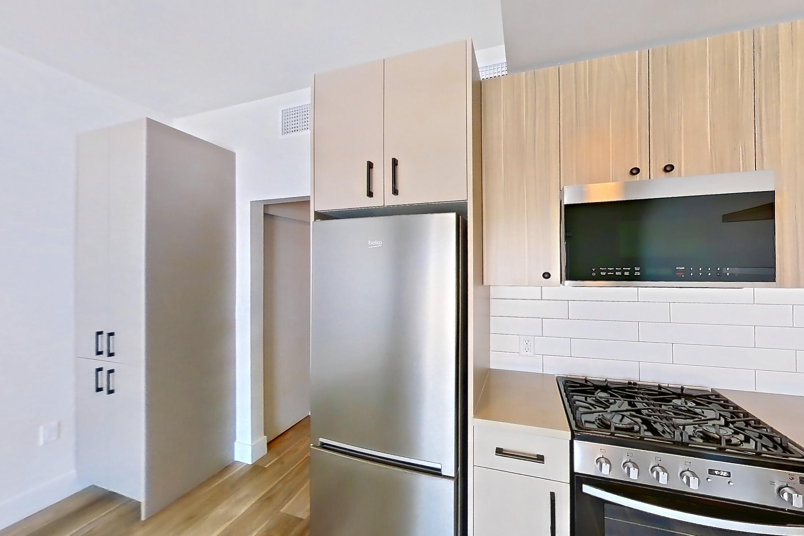 Kitchen with dishwasher, gas range, light countertops, light stone countertops, light wood-finish flooring, oven/range, refrigerator, and stainless steel appliances, Apartment 608 at The Myles