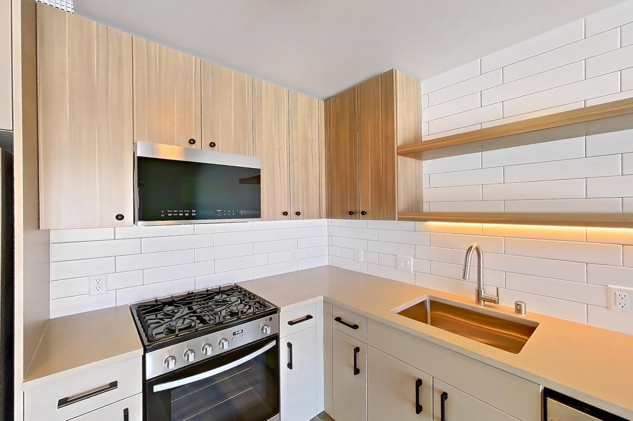 Kitchen with dishwasher, gas range, light countertops, light stone countertops, light wood-finish flooring, oven/range, refrigerator, and stainless steel appliances, Apartment 608 at The Myles