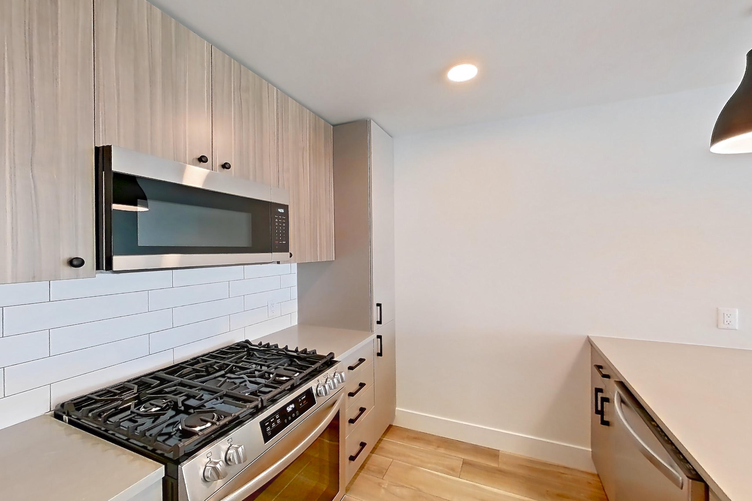 Kitchen with gas range, light countertops, light wood-finish flooring, microwave, oven/range, refrigerator, stainless steel appliances, and wood-look tile flooring, Apartment 611 at The Myles