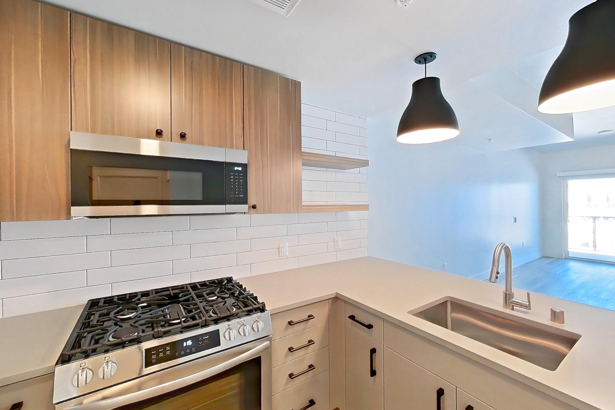 Kitchen with dishwasher, gas range, light countertops, light wood-finish flooring, microwave, oven/range, refrigerator, and stainless steel appliances, Apartment 612 at The Myles